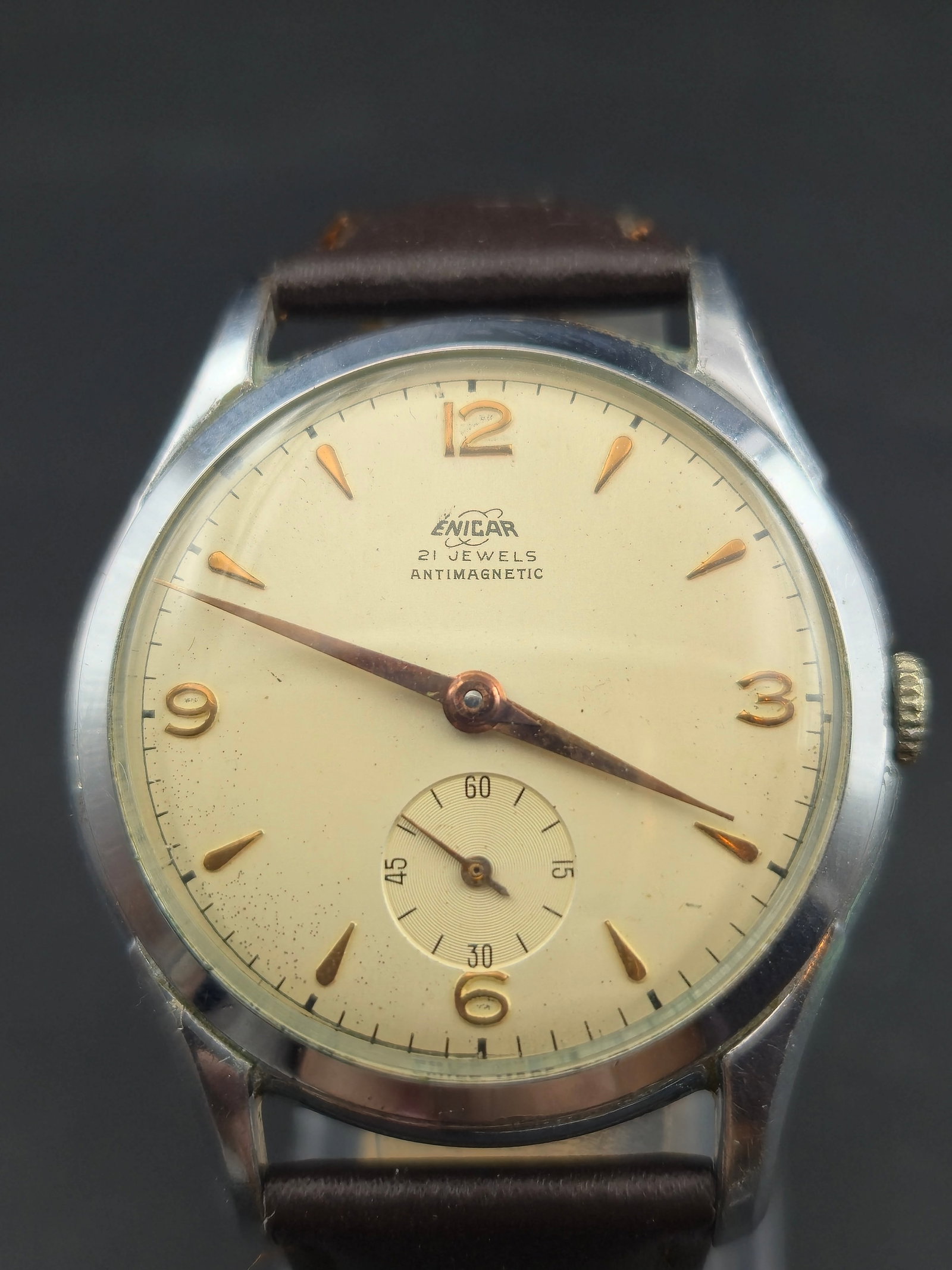 1950s Enicar Antimagnetic 38mm 21J Manual Caliber Enicar Adjusted – Running: This 1950s Enicar Antimagnetic dress watch features a classic cream dial with gold tone markers, sub seconds at six, and the Swiss Enicar twenty one jewel adjusted manual wind movement. The watch is r