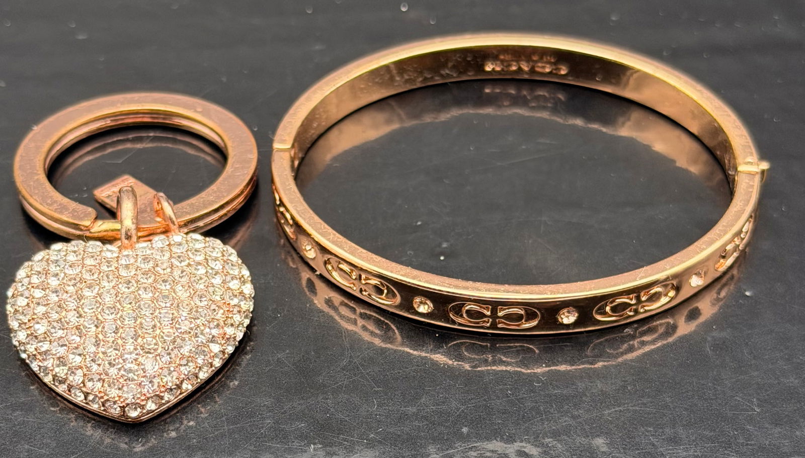 Coach Rose Gold Bracelet & Crystal Heart Keychain Set – 55g: Beautiful Coach rose-gold toned bangle bracelet with signature logo engravings and crystal accents, paired with a sparkling pavé crystal heart keychain.