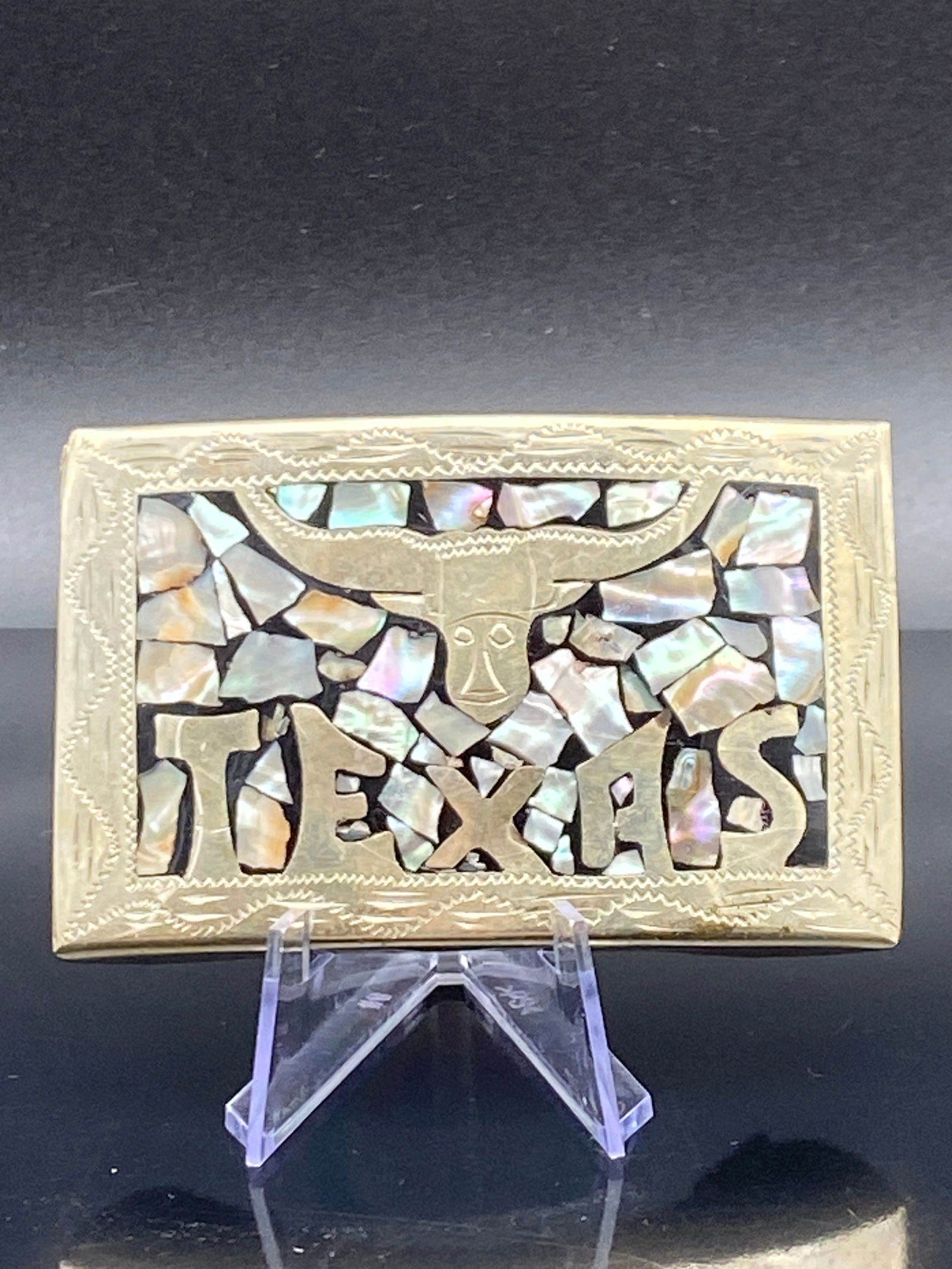 Texas Longhorn Inlay Brass Belt Buckle: A bold vintage-style brass belt buckle featuring the word “TEXAS” and a prominent longhorn cattle head motif across the center. The design is set against an eye-catching mosaic of iridescent m