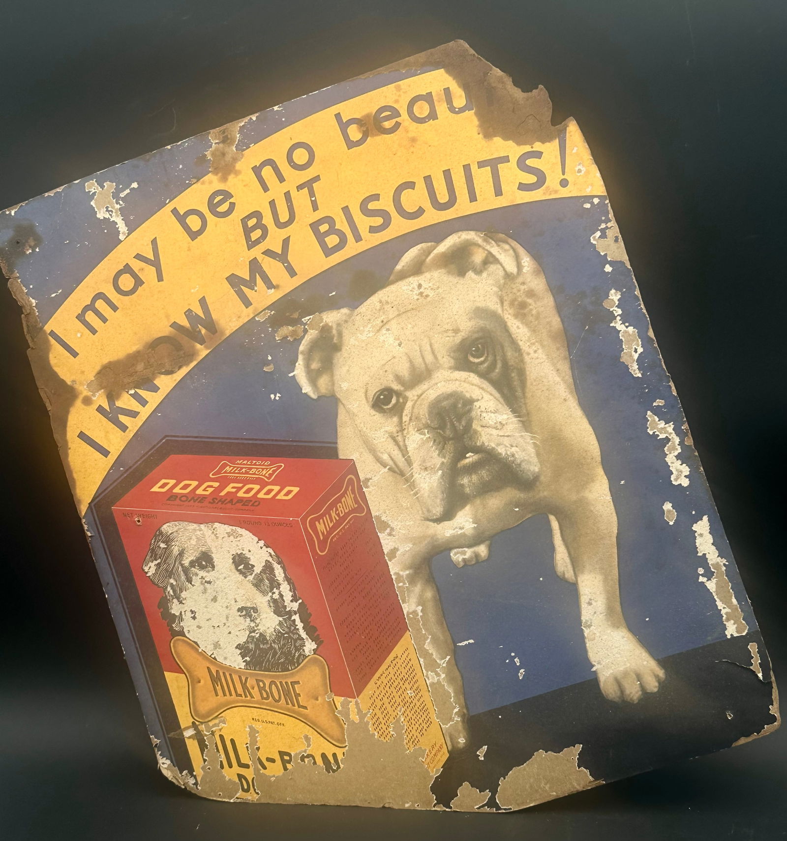 Vintage Milk-Bone Dog Biscuits Advertising Sign – Bulldog Graphic: Early lithographed cardboard advertising sign for Milk-Bone Dog Biscuits, featuring a bulldog and the classic slogan: “I may be no beaut… but I know my biscuits!” Vibrant colors remain visib