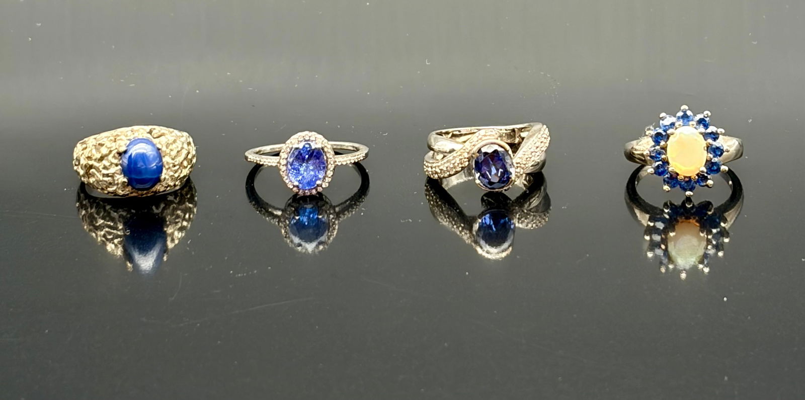 Lot of Four Blue Stone Costume Rings: Attractive assortment of four vintage-style costume rings featuring blue and opalescent stones in varied settings. Includes:• A bold gold-tone nugget-style ring set with a carved blue cabochon ce