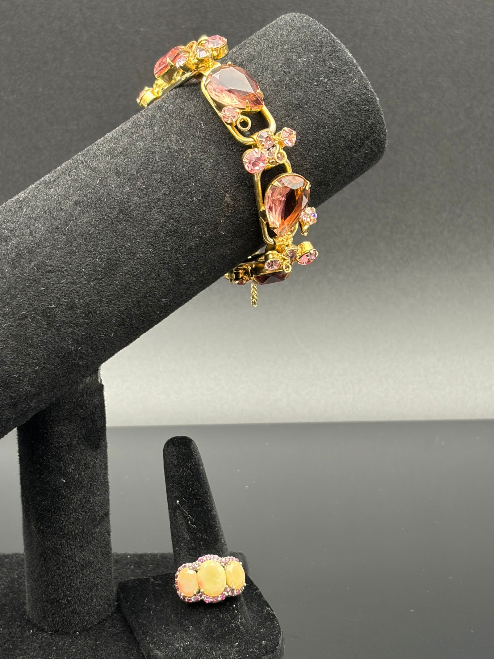 Pink Gem Bracelet & Opal-Style Ring Set: Eye-catching jewelry duo featuring a gold-tone link bracelet adorned with large pear-cut pink stones accented by clusters of smaller pink crystals. The coordinated ring showcases three oval opal-style
