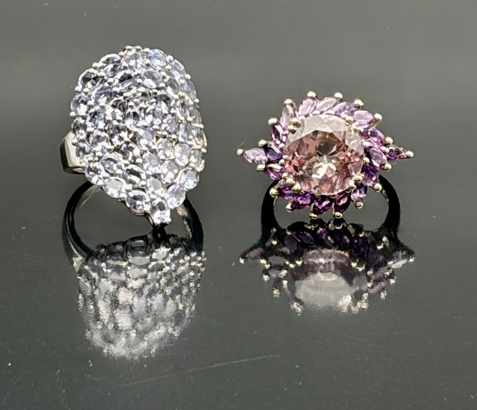 Two Statement Cocktail Rings w/ Purple Stones: Bold and glamorous duo of oversized cocktail rings, each featuring a dramatic cluster of purple and lavender stones. The first ring forms a teardrop-shaped mosaic of faceted pale lavender stones arran