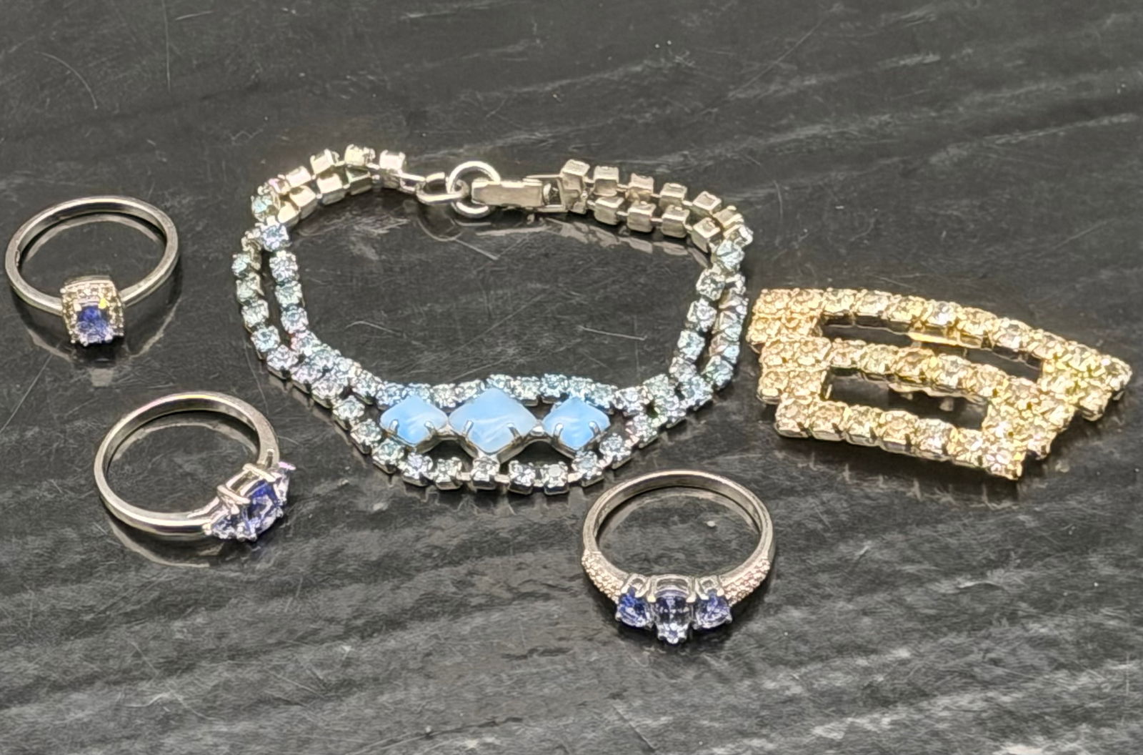 Vintage Silver & Rhinestone Jewelry Lot – Rings, Bracelet & Brooches (28g): Beautiful mixed lot of vintage rhinestone jewelry including three sterling silver 925 rings with blue/violet stones, a sparkling rhinestone bracelet, and two gold-tone rhinestone brooches.