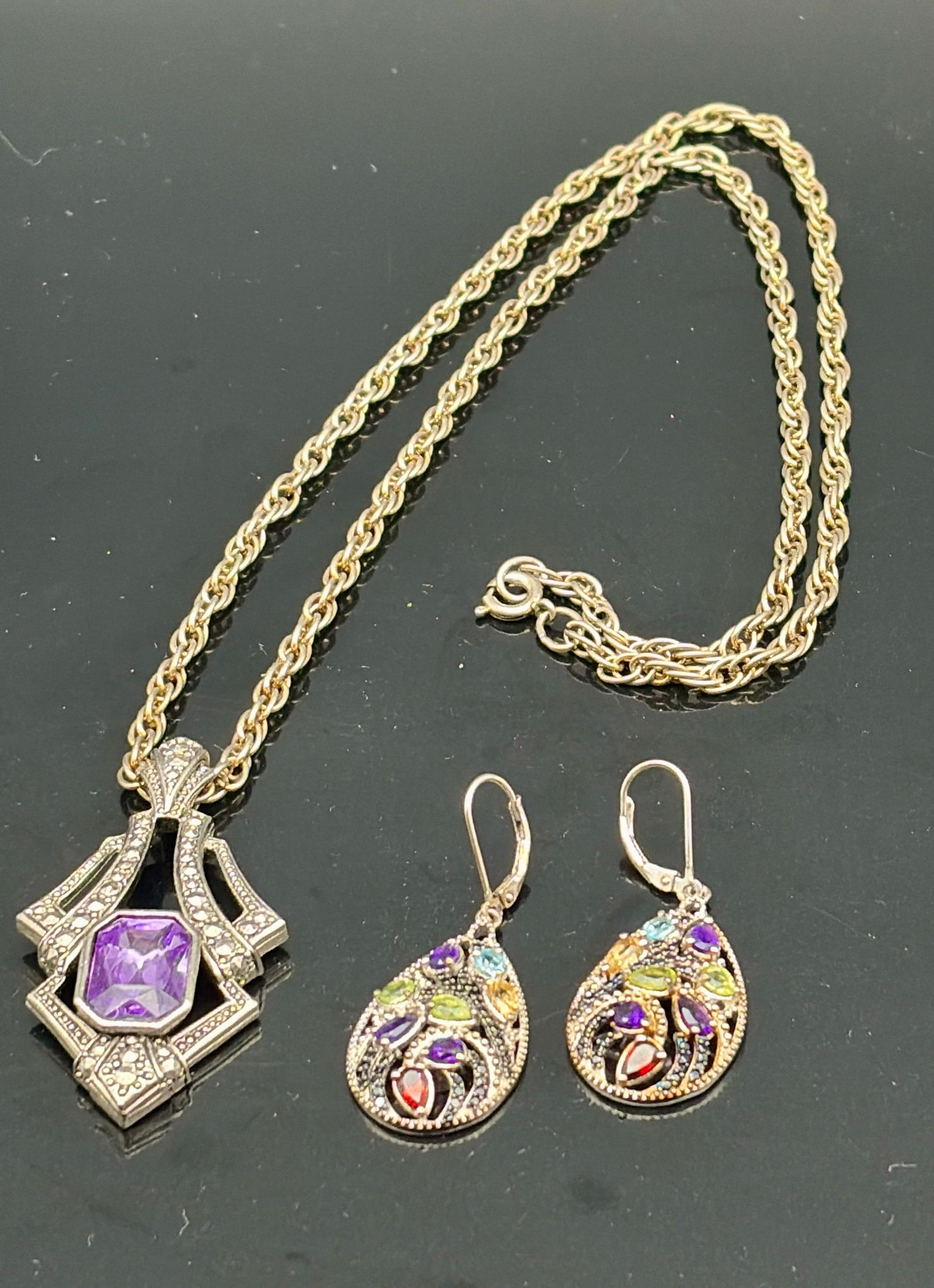 Art Deco Amethyst Pendant Necklace & Gem Earrings: Striking jewelry set featuring an Art Deco–inspired pendant necklace and a pair of ornate gemstone earrings. The pendant showcases a faceted amethyst-colored stone set within a geometric silver-tone