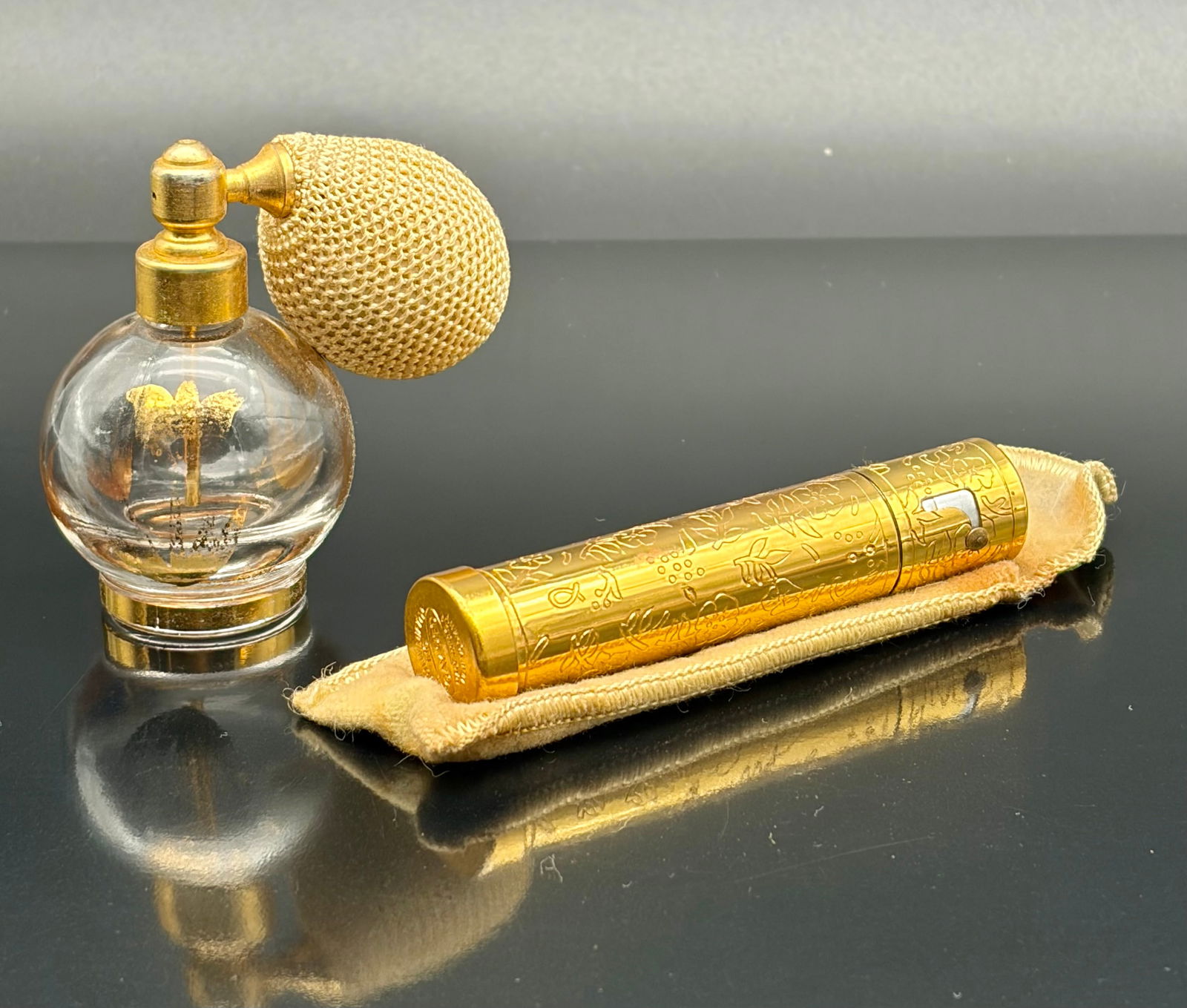 Vintage Gold-Tone Lipstick Case with Original Tube: Charming vintage lipstick holder set featuring an ornate gold-tone metal case with floral engravings, the original lipstick tube, and a fitted protective sleeve. The cylindrical case showcases intrica