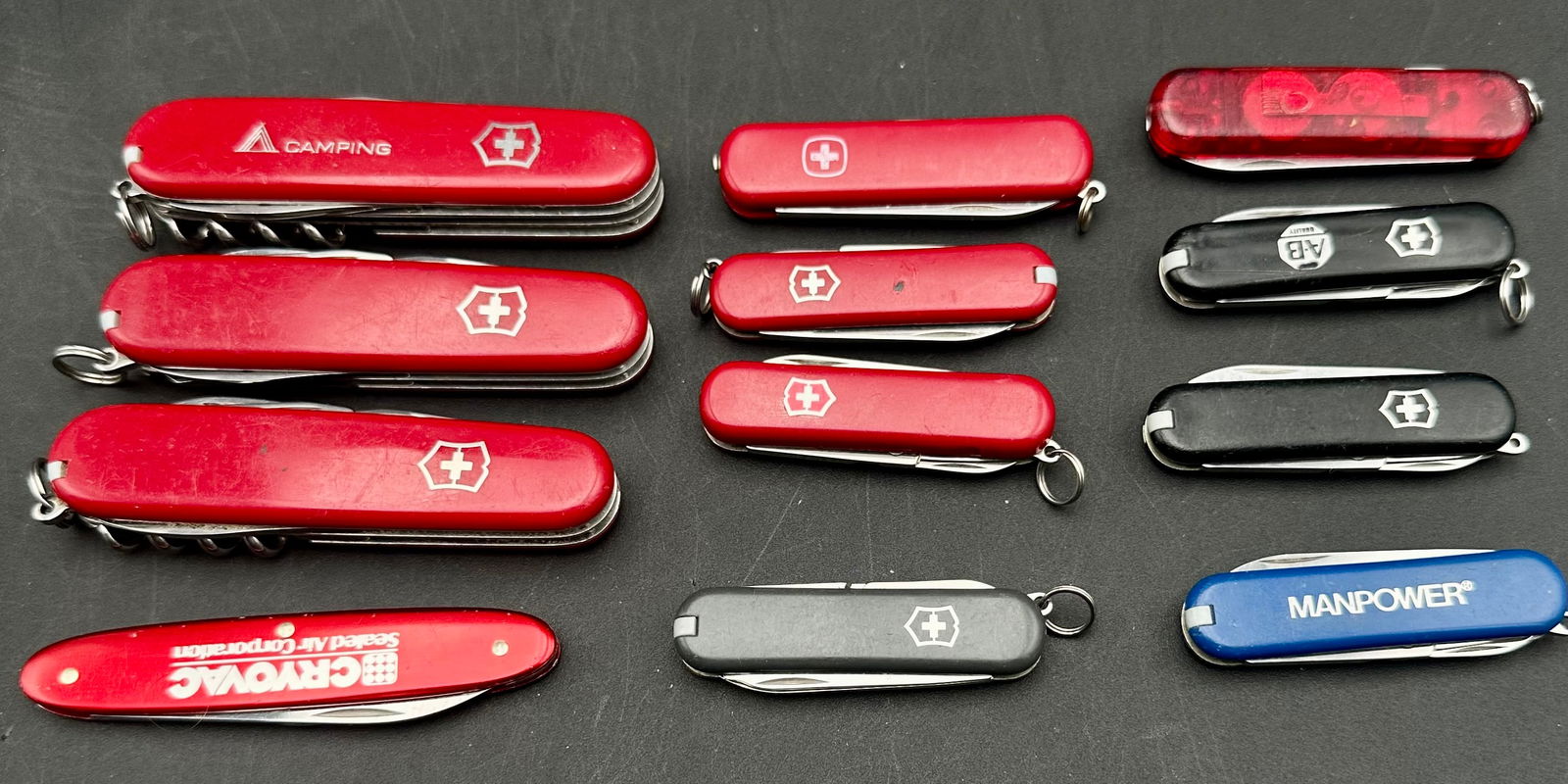 Lot of 12 Swiss Army Knives – Victorinox Wenger – Mixed Models: Lot includes 12 authentic Swiss Army pocket knives in various styles, sizes, and colors. Brands include Victorinox and Wenger with a mix of classic red, black, blue, translucent, and advertising-logo