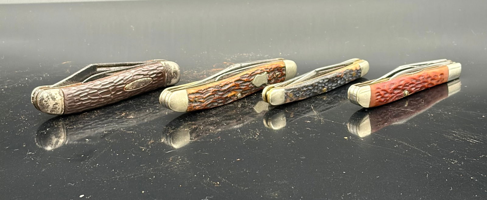 Vintage Jigged Pocket Knife: This lot includes four vintage pocket knives featuring jigged bone or jigged Delrin-style handles in brown, red, and amber tones. These knives represent classic American and mid-century import pattern