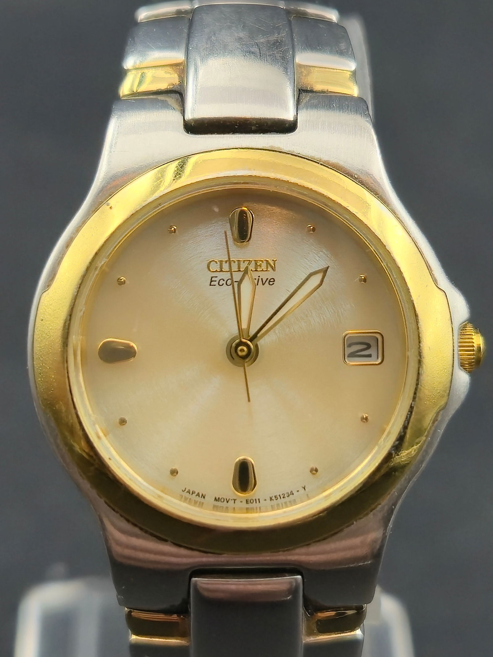 2000s Citizen Eco-Drive E011 Two-Tone 26mm Solar Quartz Watch Running & Keeping Time: Two-tone Citizen Eco-Drive E011 solar quartz watch from the early 2000s, featuring a silver sunburst dial with raised gold hour markers and a gold-framed date window. The watch is running and keeping