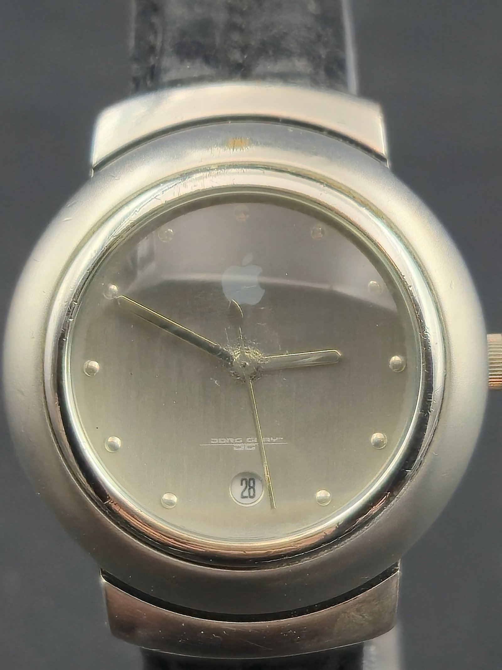 Vintage Apple Logo 29mm Grey-Logo Quartz Date Watch – Runs: This vintage Apple promotional quartz watch features the grey Apple logo on a brushed silver dial, a minimalist dot-marker layout, and a rounded modernist case. Produced as an Apple corporate giveaway