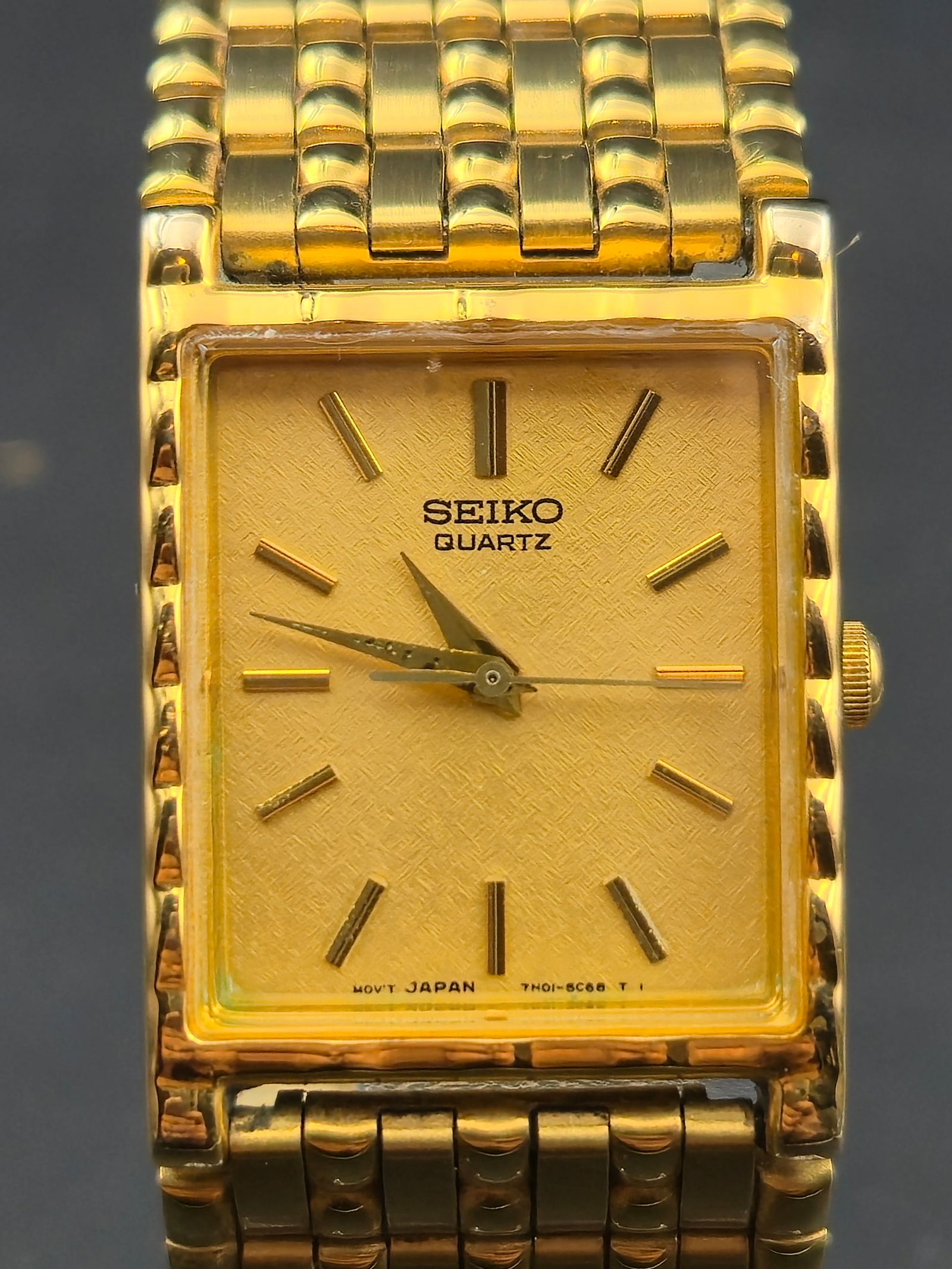 Seiko 7N01-5C39 23mm Gold-Tone Rectangular Quartz Dress Watch – New Battery: This Seiko 7N01-5C39 features a slim rectangular gold-tone case paired with an integrated multi-row bracelet, giving it a classic 1980s/1990s dress profile. The gold textured dial displays minimalist