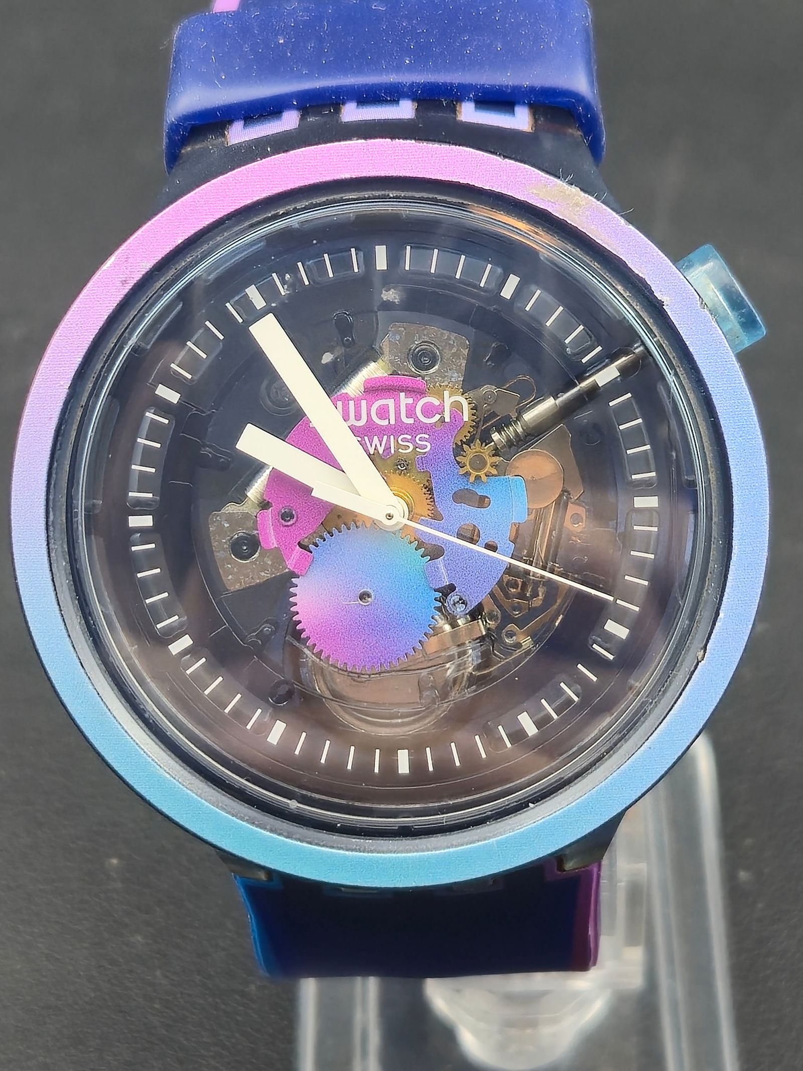 Swatch 47mm Spectrum Skeleton Blue Multicolor Quartz Watch – New Battery: This bold Swatch features a transparent blue-toned case with a full skeleton dial showcasing colorful gears in pink, purple, blue, and gold. The matching multicolor gradient strap adds to its modern s