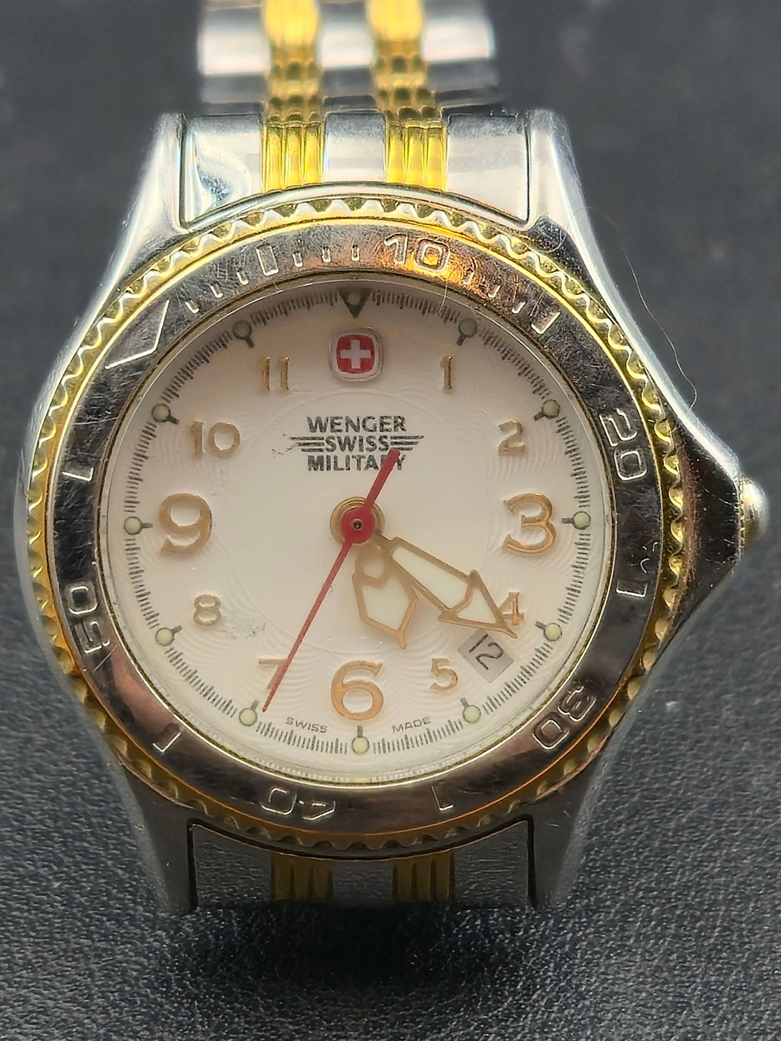 Wenger Swiss Military 79095 28mm Two-Tone 100M Quartz Watch – New Battery: This Wenger Swiss Military 79095 features a classic two-tone design with a rotating timing bezel, white textured dial, and gold-tone Arabic numerals. Built for durability, this model offers 100 meters