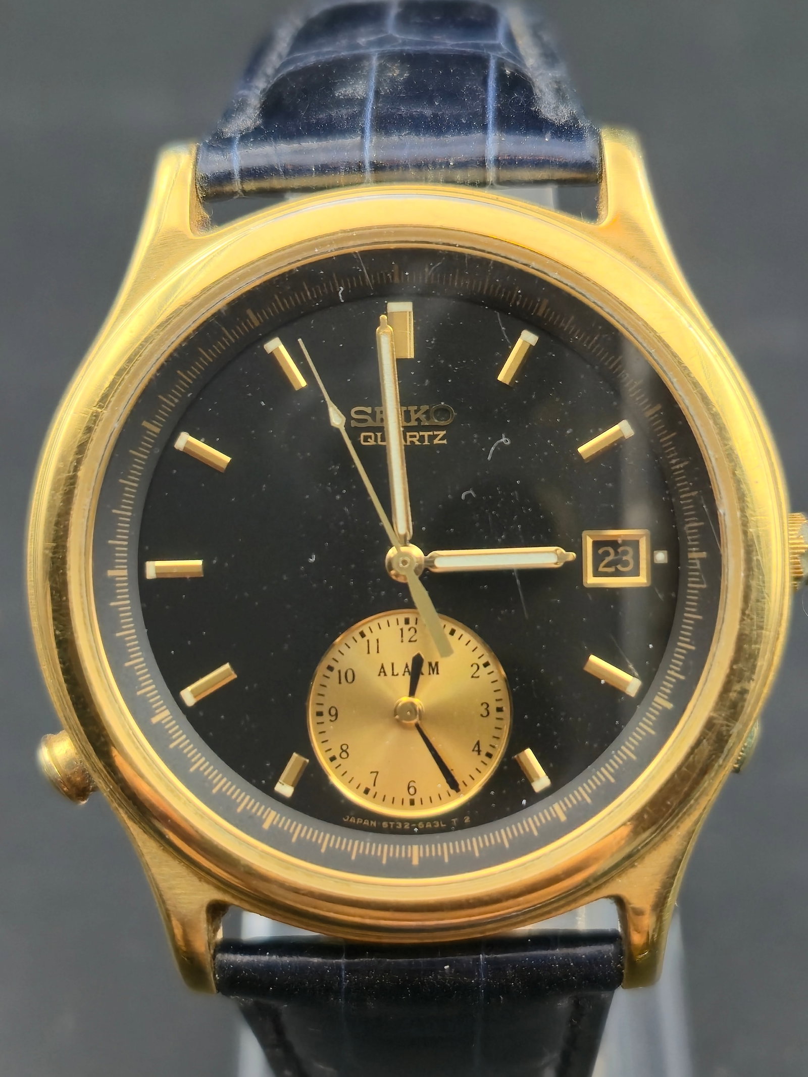 1990 Seiko 5T32 Alarm Quartz Gold-Tone Black Dial 38mm New Battery Runs: A 1990 Seiko 5T32 Alarm quartz watch featuring dual crowns, independent alarm subdial, and a classic gold-tone case paired with a dark blue crocodile-grain strap. New battery installed and running.---