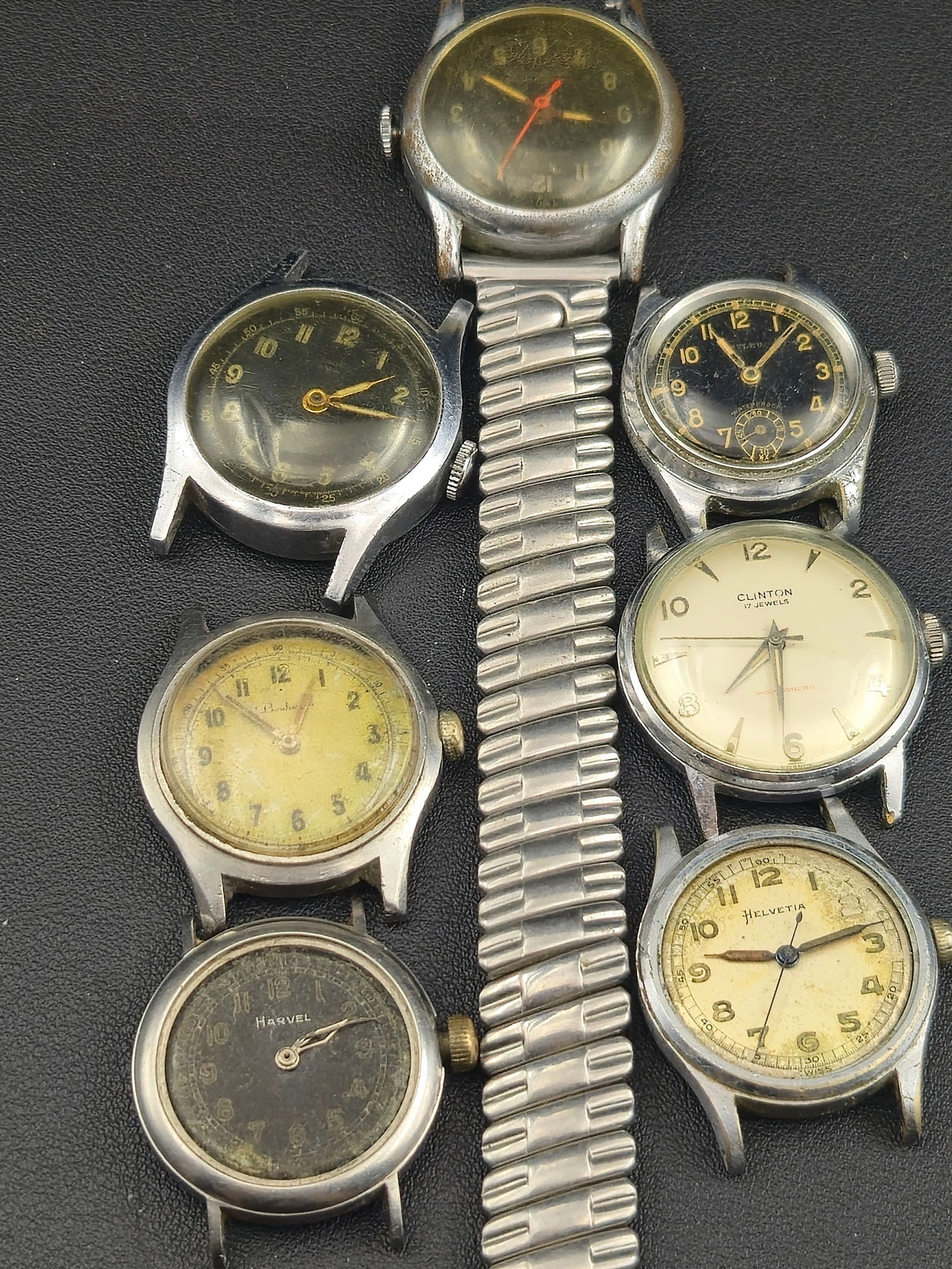 1940s–1950s Wristwatch Lot of 7 – Clinton, Helvetia, Harvel, Swiss Field Watches – Untested: mixed lot of seven vintage wristwatches from the 1940s–1950s, including Clinton, Helvetia, Harvel, and multiple Swiss field-style pieces. These watches feature classic mid-century designs, radium-er