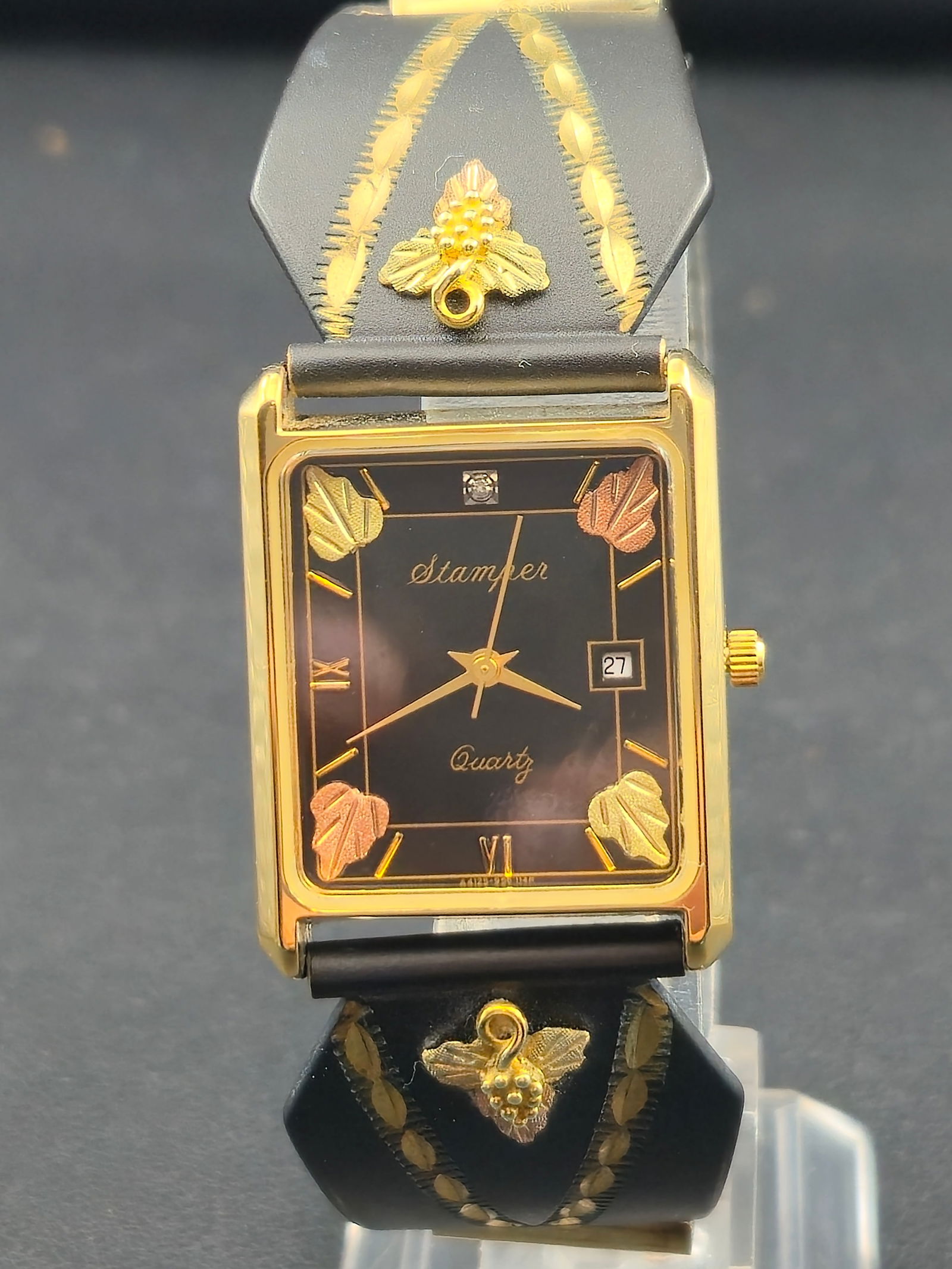 1990s Stamper Black Hills Gold 25mm Quartz Watch New Battery Runs: A distinctive 1990s Stamper Black Hills Gold quartz wristwatch featuring the brand’s signature tri-color gold leaf accents on both the dial and bracelet. The glossy black rectangular dial includes g
