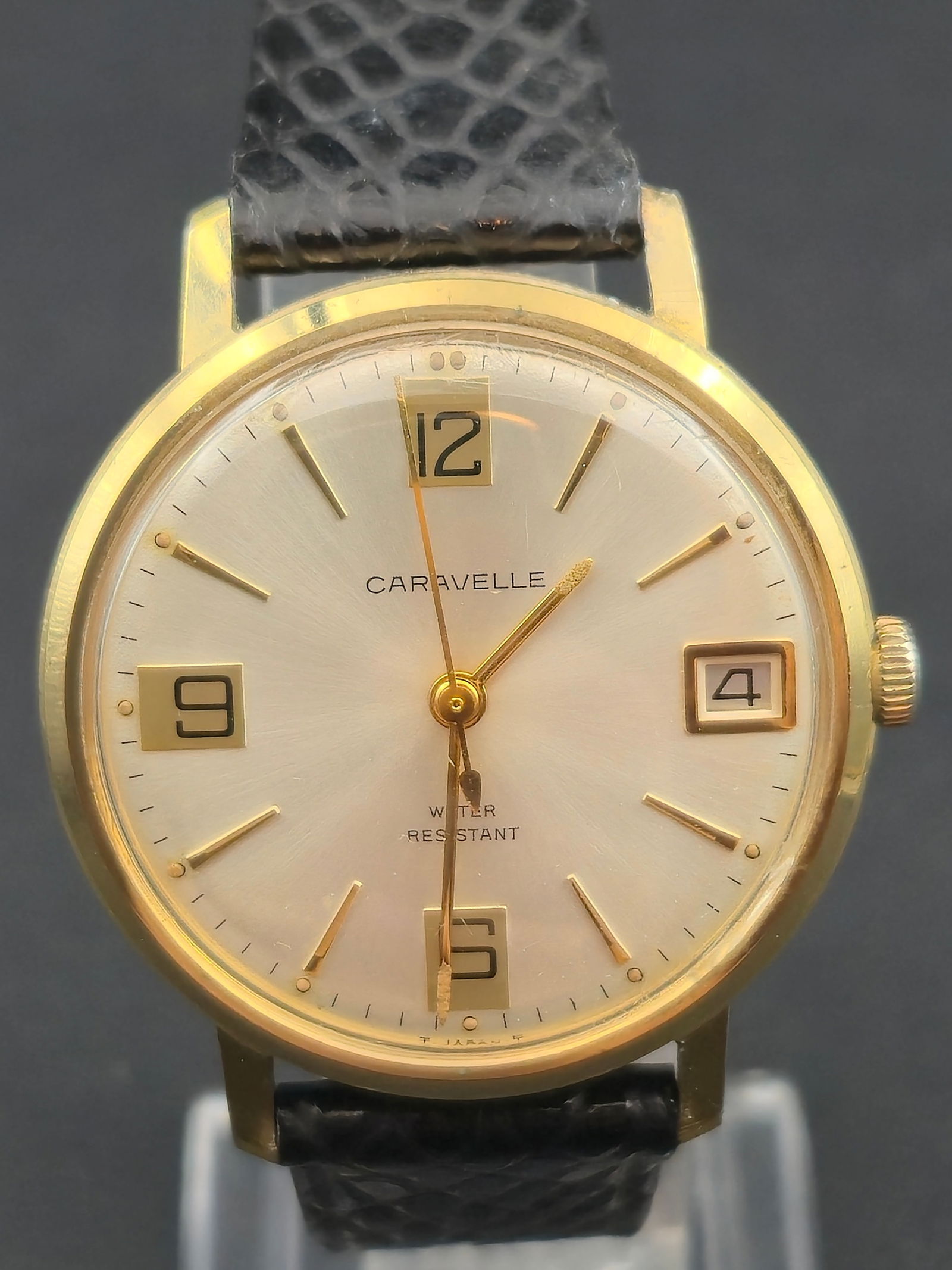 Caravelle by Bulova 7J Manual Wind Wristwatch c.1960s 35.1mm Runs: Vintage Caravelle by Bulova manual-wind wristwatch featuring a clean silver sunburst dial with applied gold-tone markers, framed Arabic numerals, and date window at 3 o’clock. Gold-tone base metal b