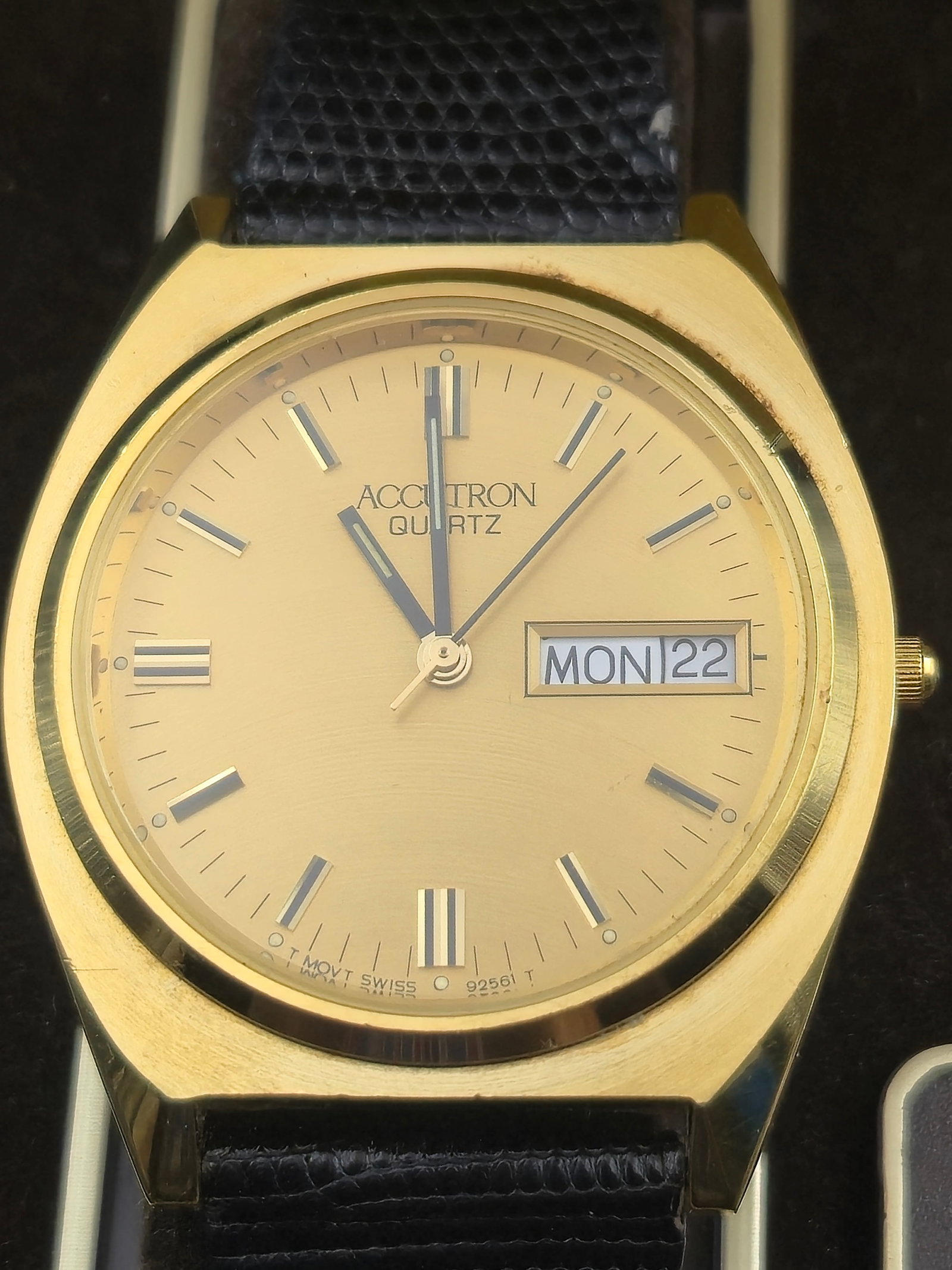 Accutron Quartz Day-Date Watch Gold Tone Case 35.4mm Swiss Movt Leather Strap Bulova Box New Battery: Accutron quartz day-date wristwatch with gold-tone dial, applied baton markers, and matching gold-tone hands. Day window at 3 o’clock showing MON and date window showing 22 at time of photography. G