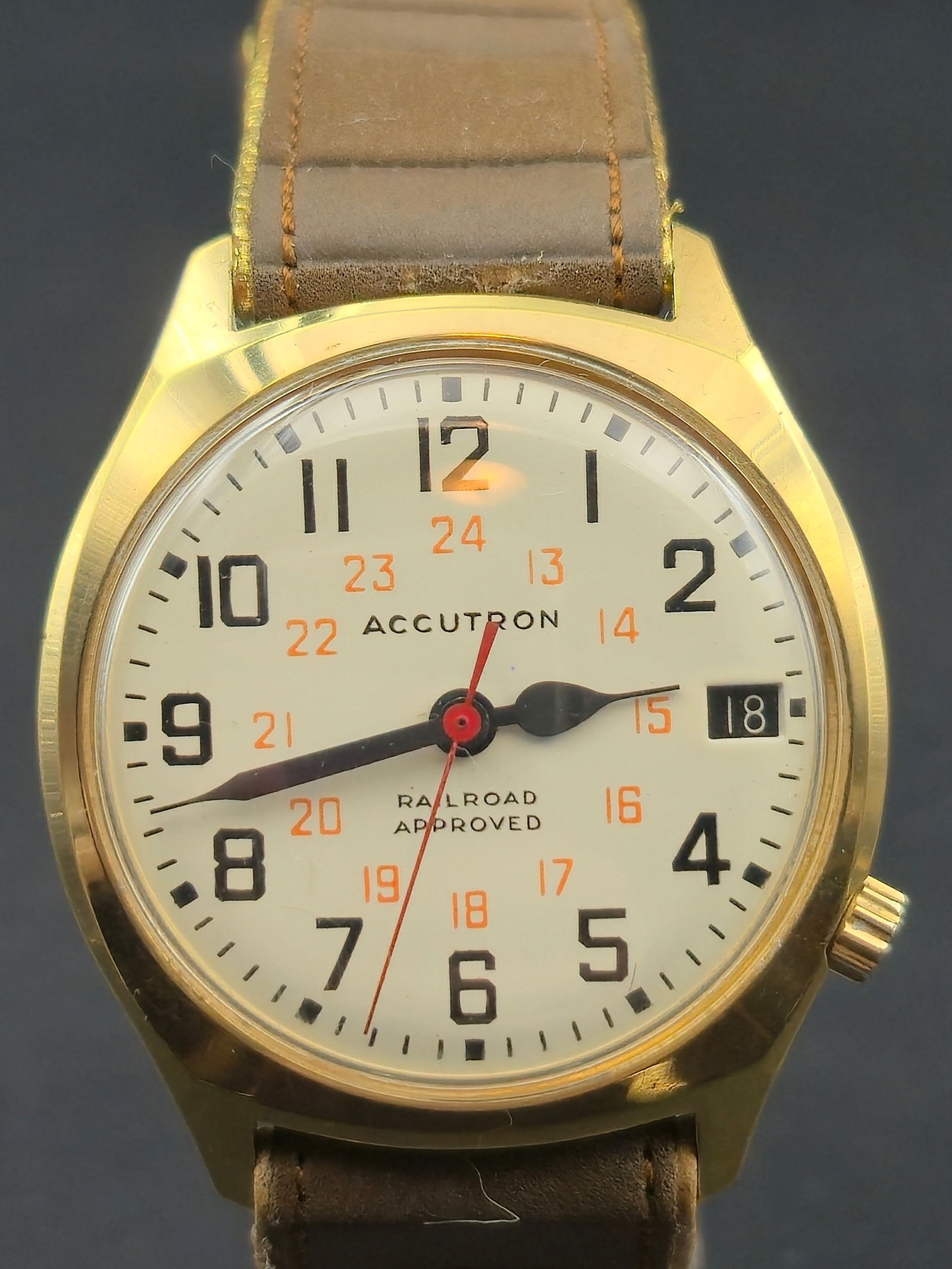 1975 Bulova Accutron 2181 Gold Electroplate Case Railroad Dial Date 33.46mm: Bulova Accutron wristwatch with white railroad-style dial. Dial reads ACCUTRON and RAILROAD APPROVED, with black Arabic numerals, inner 24-hour track in orange, red sweep seconds hand, and date window