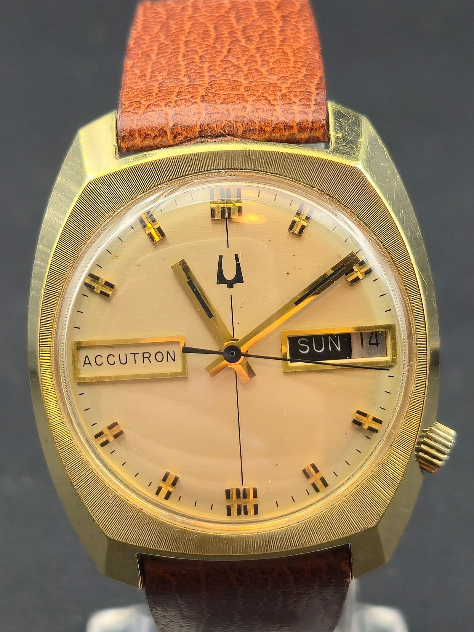 1976 Bulova Accutron 2193.10 Gold Electroplate Case Day Date Champagne Dial 33.57mm: Bulova Accutron wristwatch with champagne-tone dial. Dial reads ACCUTRON and features applied gold-tone baton hour markers with tuning fork logo. Day-date display at 3 o’clock showing SUN 14. Gold e