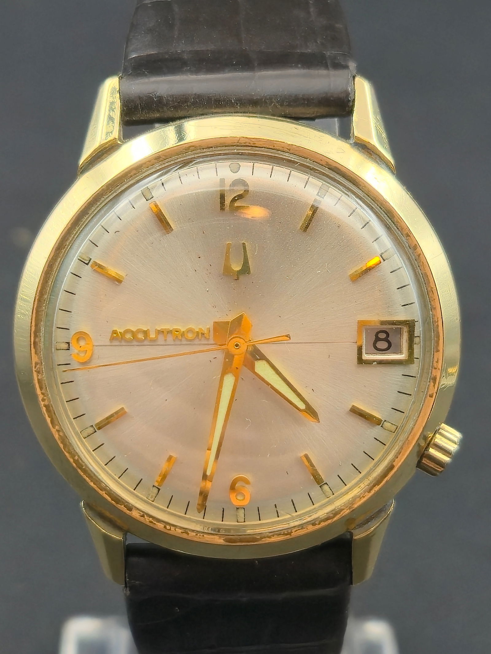 1972 Bulova Accutron 2181 14K Gold Filled Case Silver Dial Date 34.21mm: Bulova Accutron wristwatch with silver sunburst dial. Dial reads ACCUTRON and features applied gold-tone baton hour markers with Arabic numerals at 12, 9, and 6, tuning fork logo beneath 12, and a fra