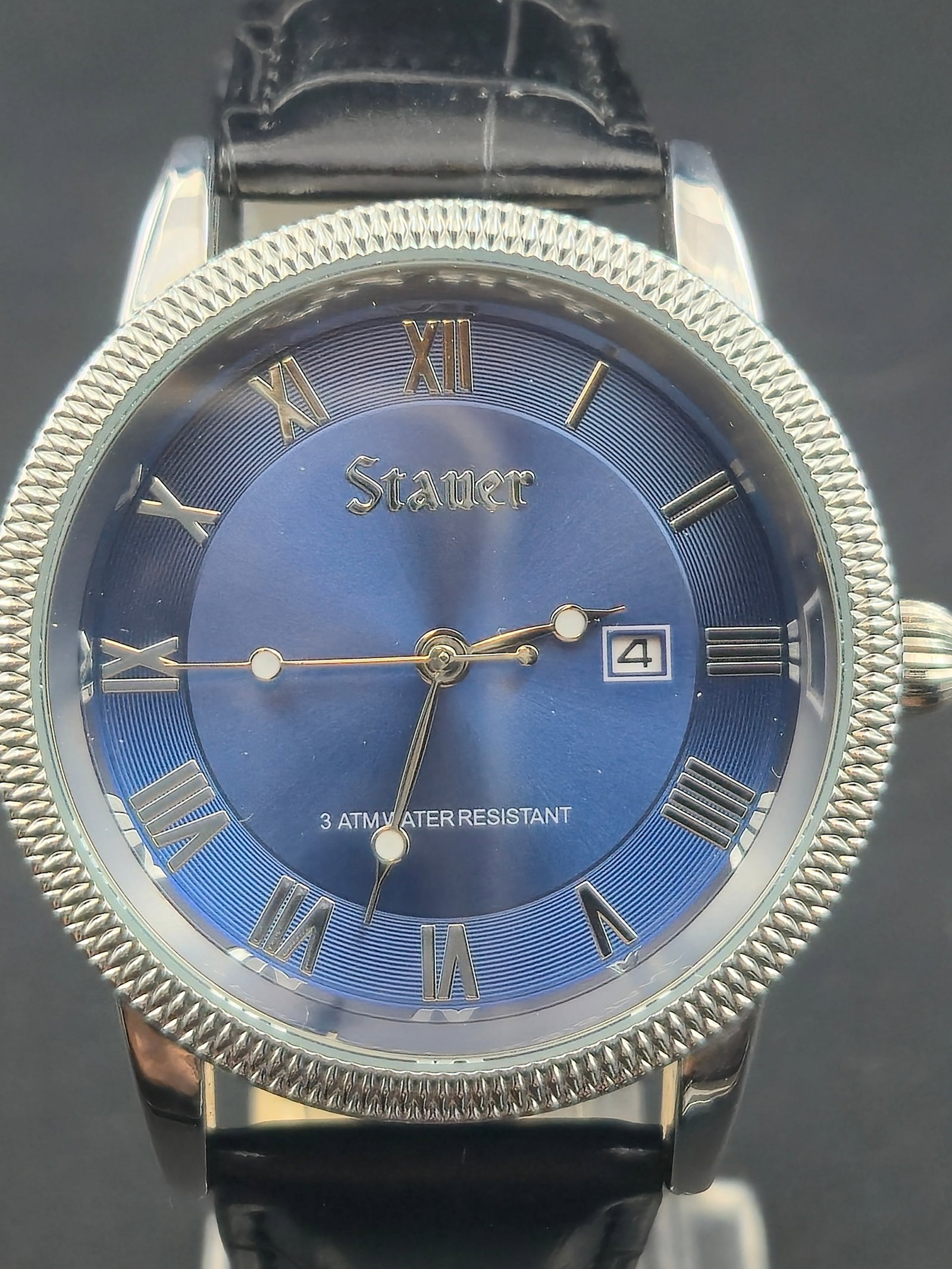 Stauer Modern Quartz Watch Blue Roman Dial Date 43mm Coin Edge Bezel New Battery: Modern-era Stauer quartz wristwatch featuring a blue sunburst dial with applied Roman numerals and a date window at 3 o’clock. Coin-edge bezel and onion-style crown give a classic dress appearance.