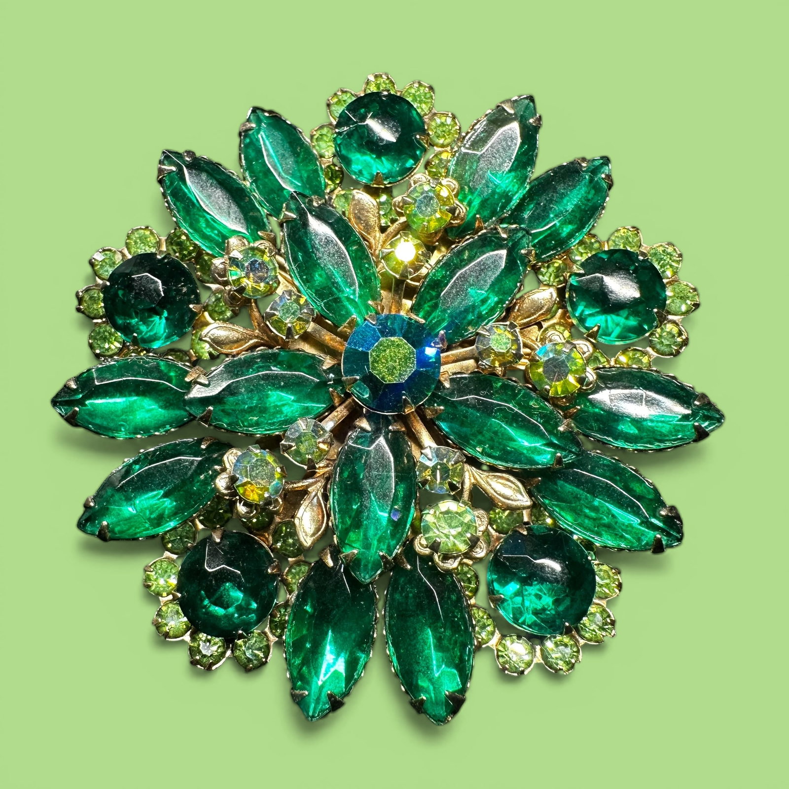 27g Faceted Green Rhinestone Gold Tone Brooch: 27g 2.31” Faceted Green Rhinestone Gold Tone Brooch:Brand/Model: Unknown brand.Manufacturer Location: Not marked.Year Produced: Unknown.Condition: Good vintage condition with light surface wear