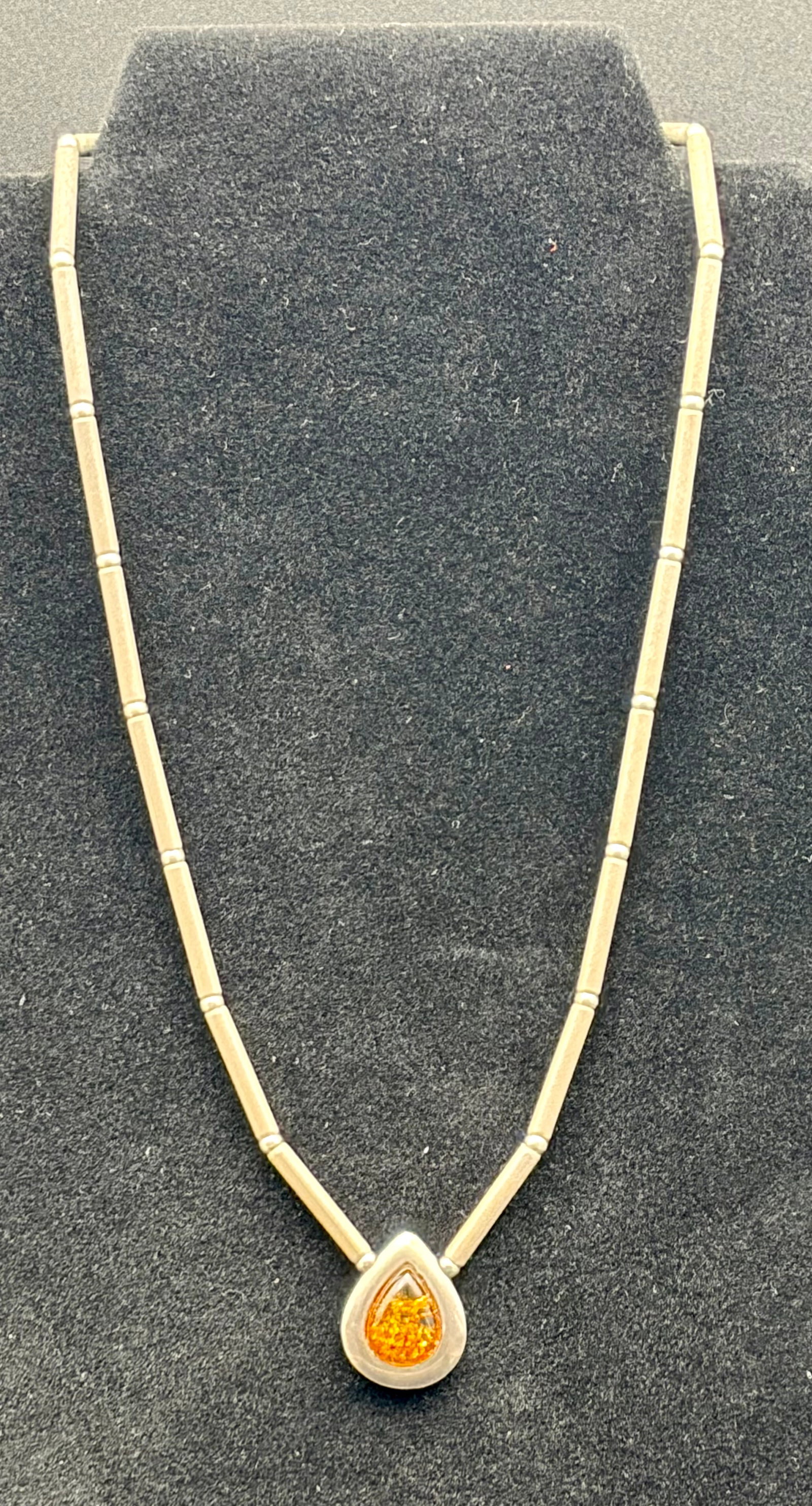 Vintage Sterling Silver Necklace with Amber Teardrop Pendant – Modernist Style: An elegant vintage necklace crafted in sterling silver, featuring a sleek articulated tube-link chain and a striking teardrop pendant set with warm honey-colored amber. The pendant’s organic, fluid