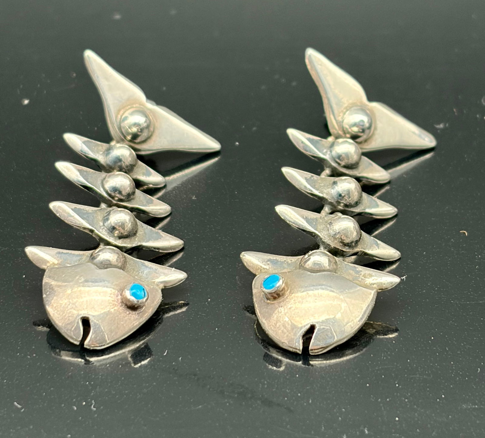 Sterling Silver Articulated Fish Earrings with Turquoise Eyes – Artisan Statement Dangles: A striking and playful pair of artisan-crafted sterling silver earrings in the form of articulated fish. Each earring features a stylized fish head with a vivid turquoise eye, followed by a chain of i