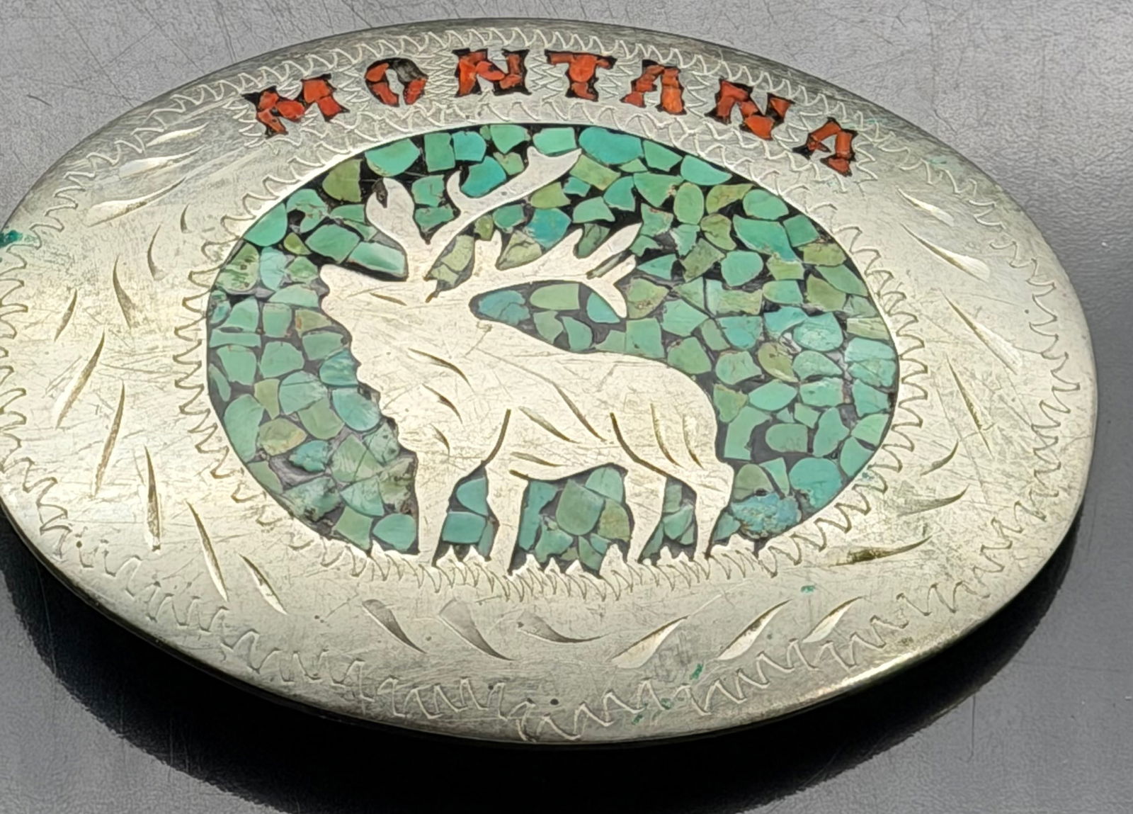 Vintage Montana Sterling Silver Turquoise Inlay Elk Belt Buckle – 130g: Large vintage sterling silver belt buckle featuring a detailed elk/deer motif set against a turquoise chip inlay background. The top is accented with “Montana” lettering in red stone inlay.