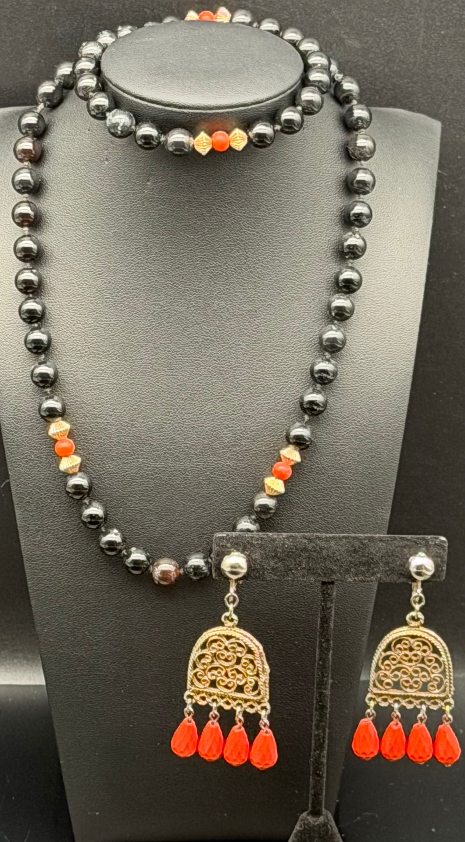 Black Beaded Necklace & Filigree Dangle Earrings Set – 60g: Elegant matching jewelry set featuring a long black beaded necklace accented with gold-tone spacers and vibrant red beads. Paired with ornate gold-tone filigree dangle earrings adorned with red drop a