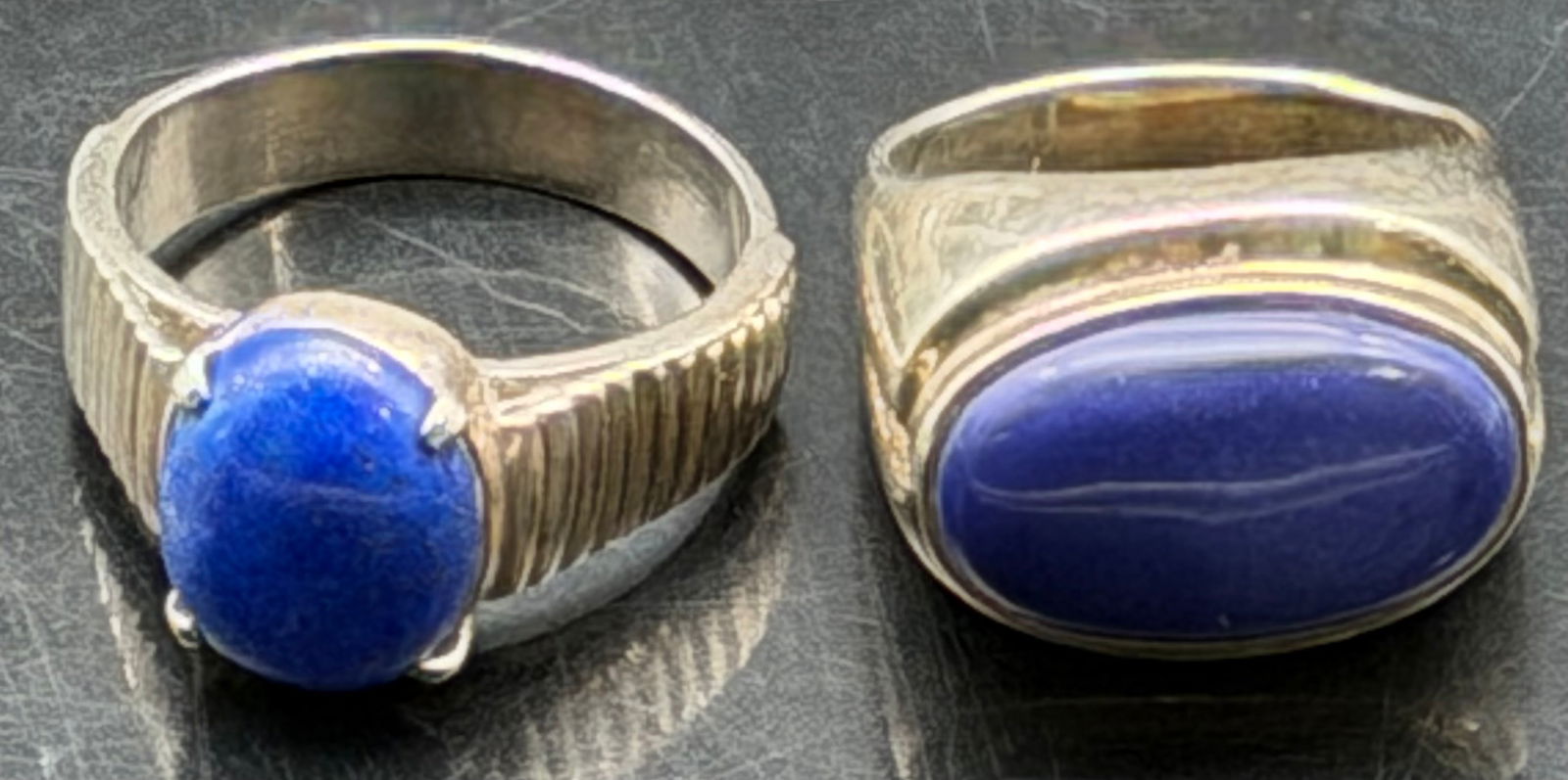 Sterling Silver Blue Stone Men’s Rings Lot of 2 – 20g: Lot of two vintage sterling silver men’s rings featuring oval blue cabochon stones. One ring has a ribbed shoulder design with prong-set blue stone, the other is a smooth signet-style setting with o