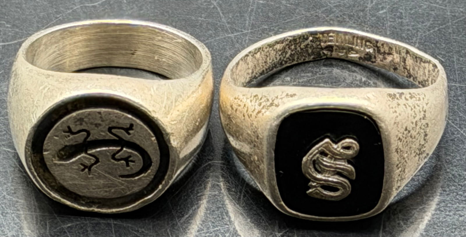 Mexican Sterling Men’s Rings Lot – 21g: Lot of two vintage Mexican men’s sterling silver rings, total weight 21 grams. One features a lizard/gecko motif signet face, the other a black inlay panel with raised serpent “S” design.