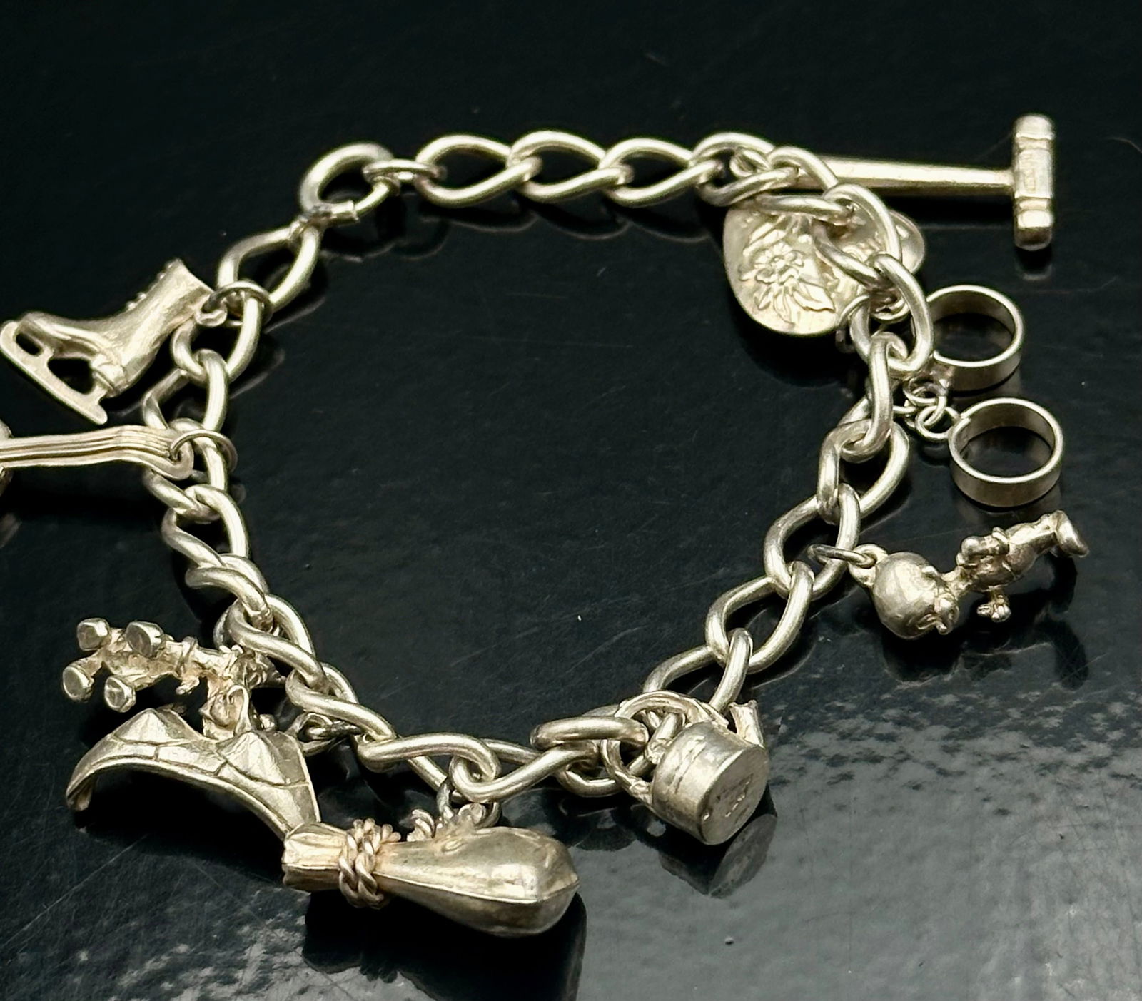 Vintage Sterling Silver Charm Bracelet – 27g: Vintage sterling silver charm bracelet featuring a toggle clasp and multiple dangling novelty charms including a Sekine heart charm, rings, shoe, and whimsical figural accents. Attractive vintage brac