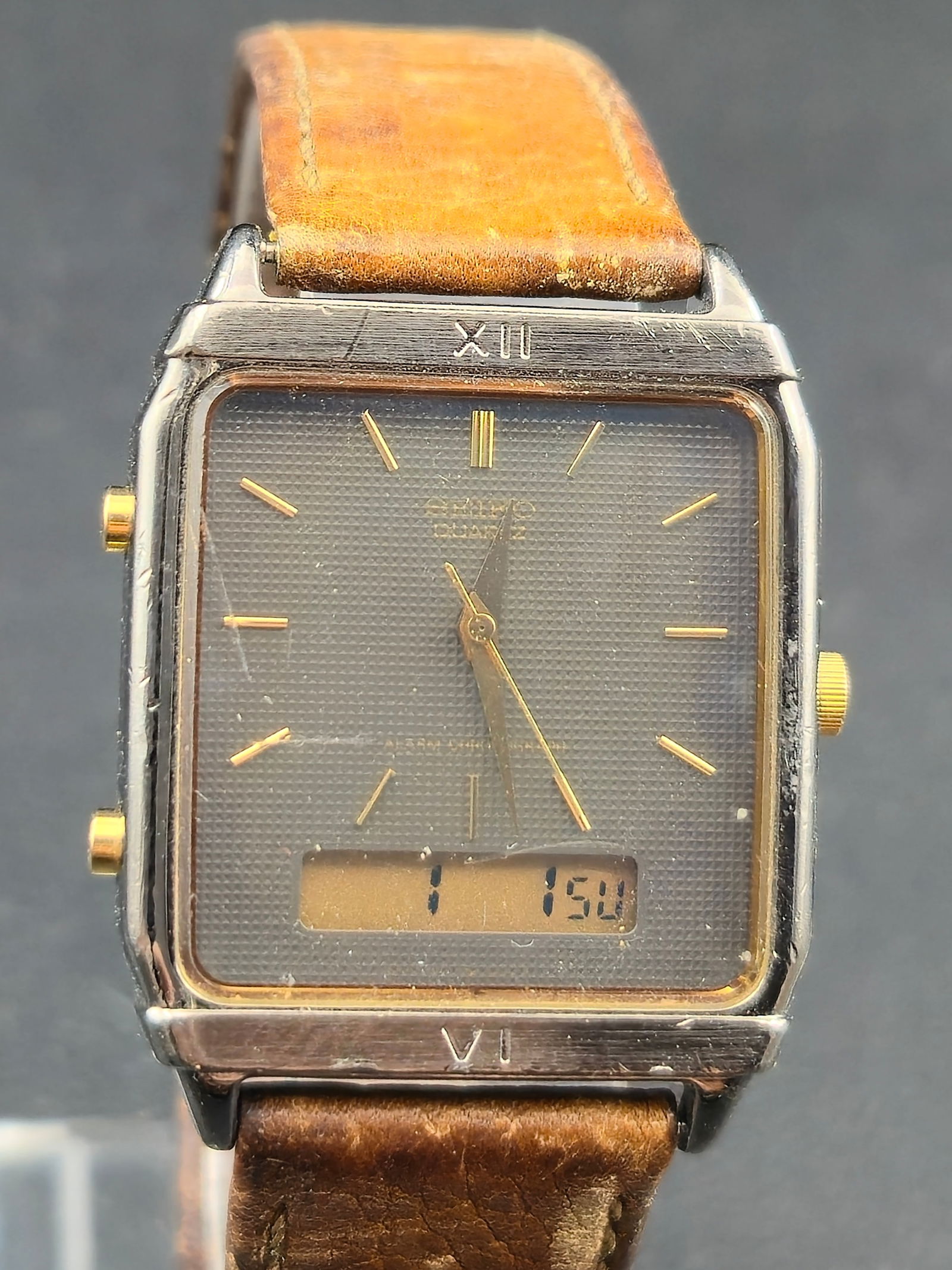 Seiko Quartz Ana Digi Rectangular Wristwatch Base Metal Stainless Back 28mm circa 1980s: Seiko quartz analog-digital wristwatch featuring a rectangular gray textured dial with gold-tone baton hour markers and matching gold-tone hands. Integrated digital display at 6 o’clock with push-bu