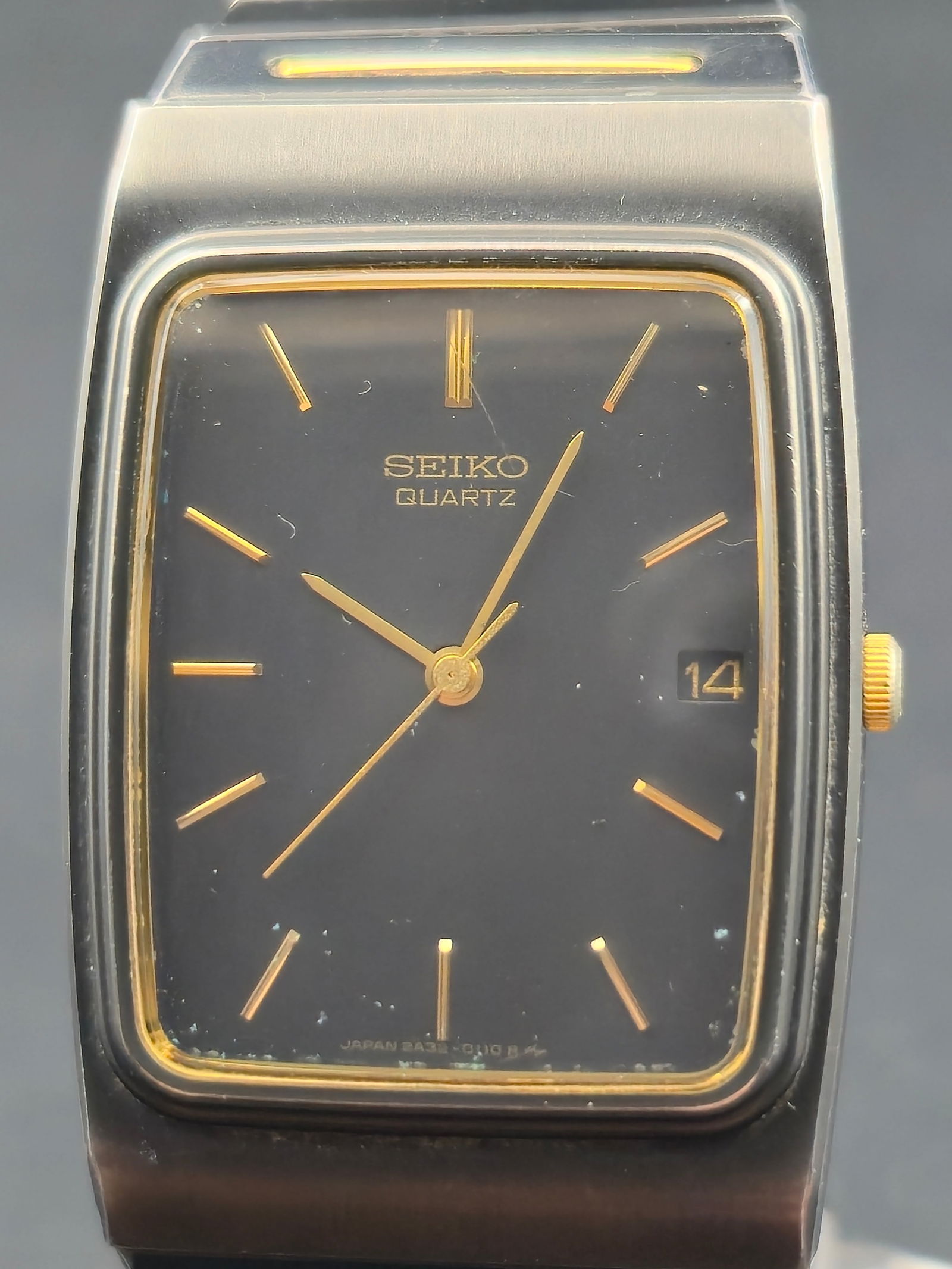 Seiko Quartz Rectangular Wristwatch Black Dial Two Tone Bracelet 26mm Ref 2A32 5059 circa 1980s: Vintage Seiko quartz rectangular wristwatch featuring a black dial with applied gold-tone baton hour markers and matching gold-tone hands. Dial signed Seiko Quartz with date window at 3 o’clock. Sli
