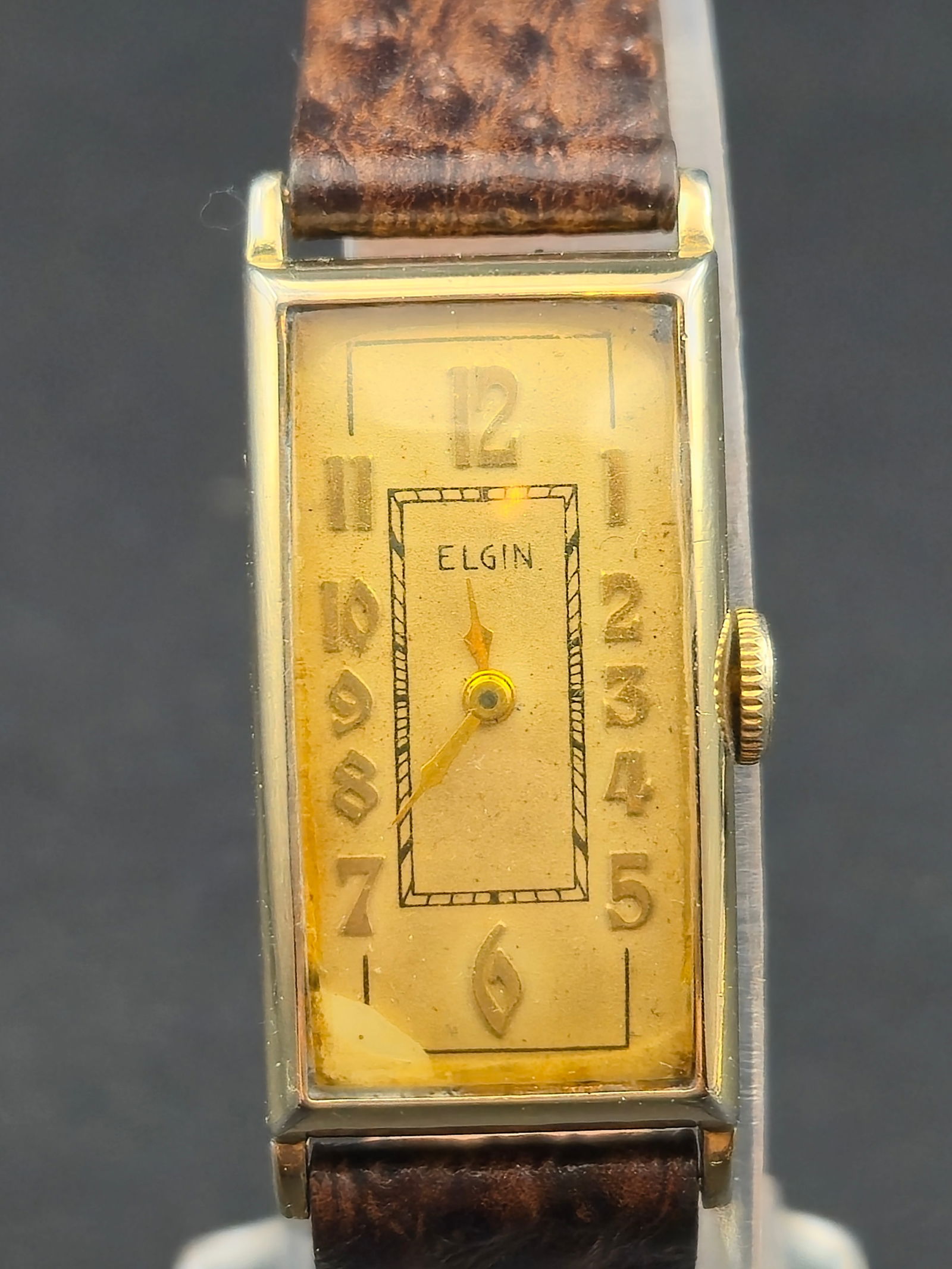 1930s Elgin Rectangular Gold Tone Wristwatch Runs 17mm Vintage: Vintage Elgin rectangular wristwatch featuring a cream dial signed Elgin with applied Arabic numerals and gold-tone hands. Slim rectangular case with gold-tone finish over base metal, paired with a br