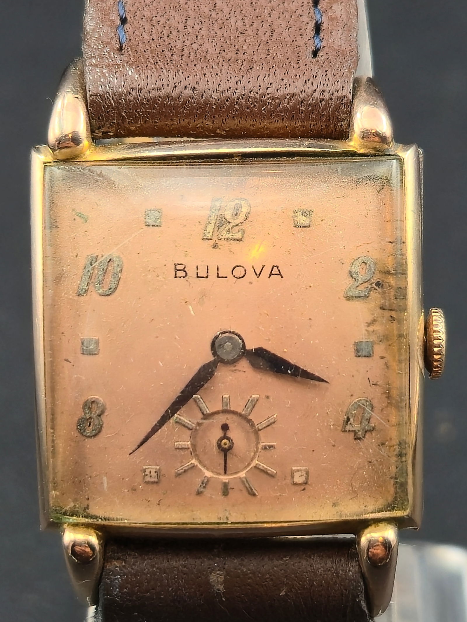1940s Bulova Rectangular Wristwatch 14K Rose Gold Plate Runs: Vintage Bulova rectangular wristwatch from the 1940s, featuring a warm rose-toned dial signed Bulova with applied Arabic numerals and a small seconds subdial at 6 o’clock. Classic mid-century rectan