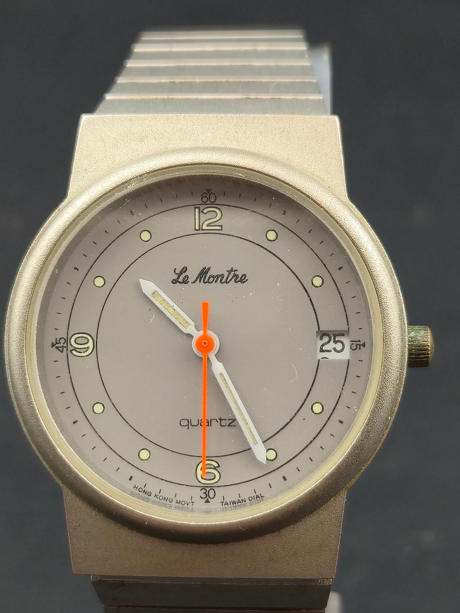 1980s Le Montre Quartz Date Wristwatch 32mm grey Tone Case Stainless Back Runs: Vintage Le Montre quartz wristwatch from the 1980s featuring a minimalist gray dial with luminous dot markers, bold orange seconds hand, and date window at 3 o’clock. Dial is marked Quartz with Hong