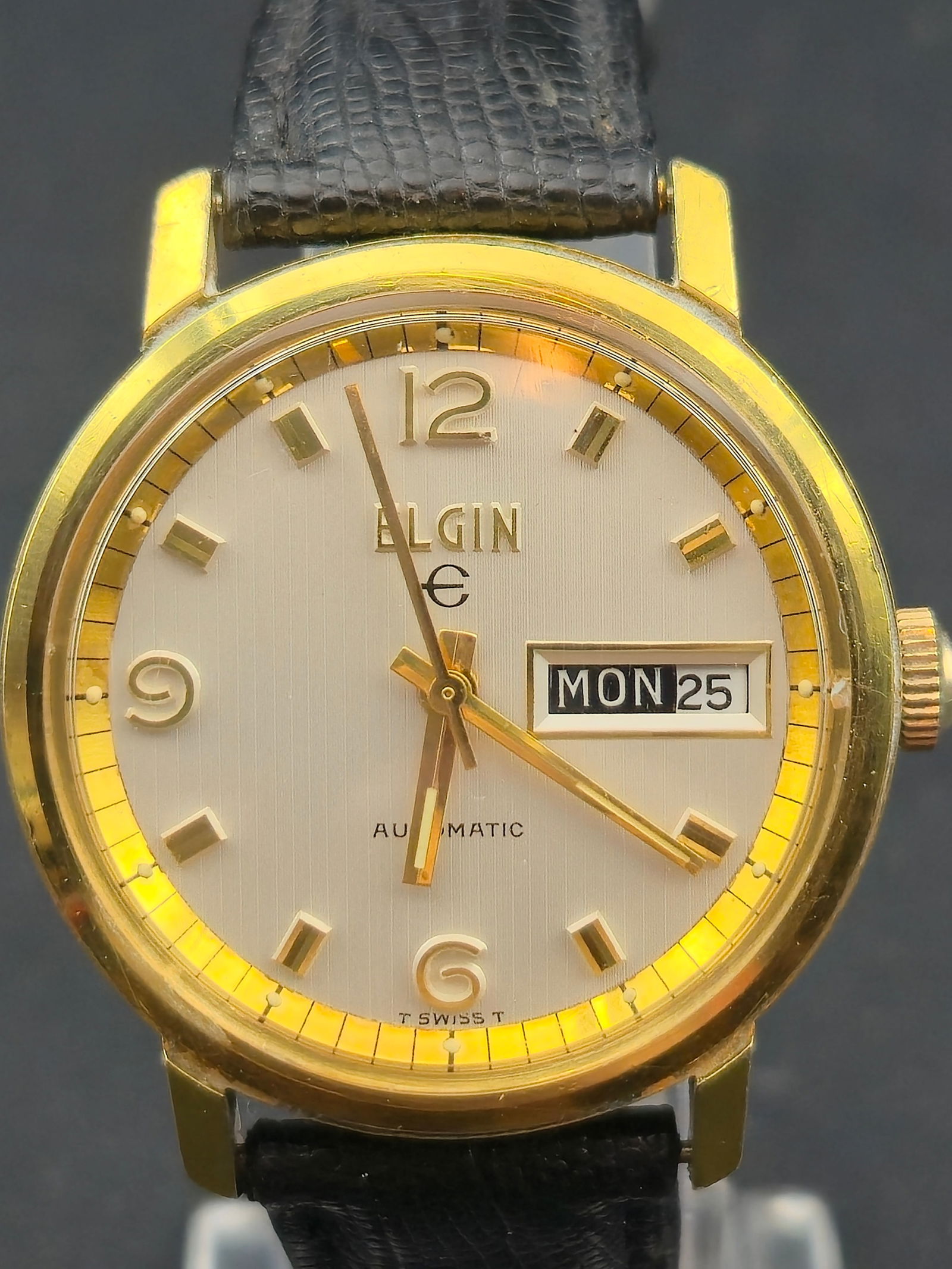 1970s Elgin Automatic Cal 334 Gold Tone Stainless Back 35mm Day Date Watch Running: Vintage Elgin automatic wristwatch featuring a silver-tone vertically brushed dial with applied gold-tone hour markers and matching hands. Dial is signed ELGIN with AUTOMATIC and a framed day-date win