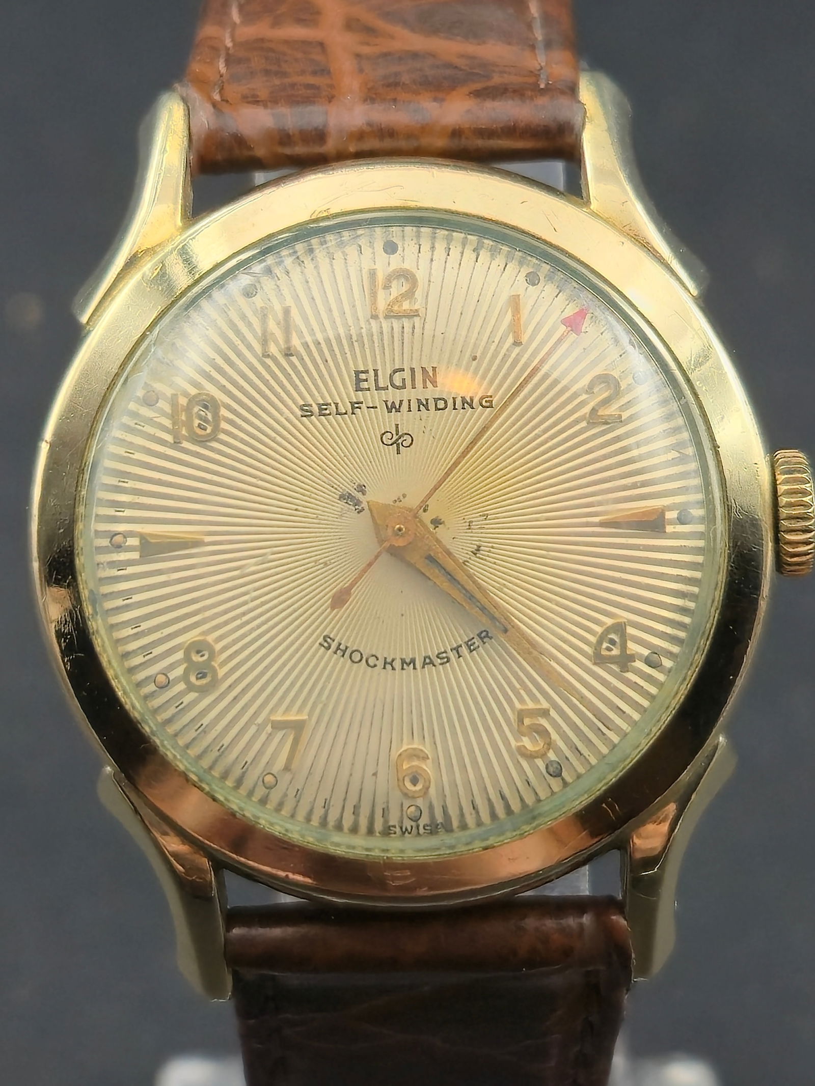 1950s Elgin Shockmaster 643 17J Self Winding 10K Gold Filled 33mm: Vintage 1950s Elgin Shockmaster self-winding wristwatch featuring a striking silver sunburst dial with applied gold Arabic numerals and arrow markers. The dial is signed ELGIN Self-Winding and Shockma