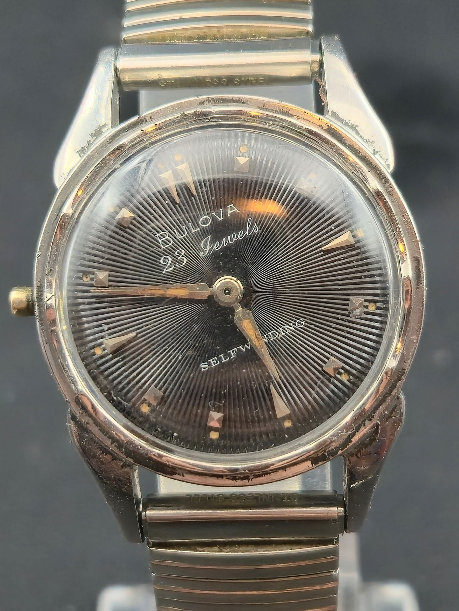 1950s Bulova 23 Jewels Self Winding 30mm Stainless Steel Black Dial Swiss Watch: Vintage 1950s Bulova self winding wristwatch featuring a black radial textured dial with applied gold tone arrow and pyramid markers. Dial marked “Bulova 23 Jewels” and “Self Winding.”