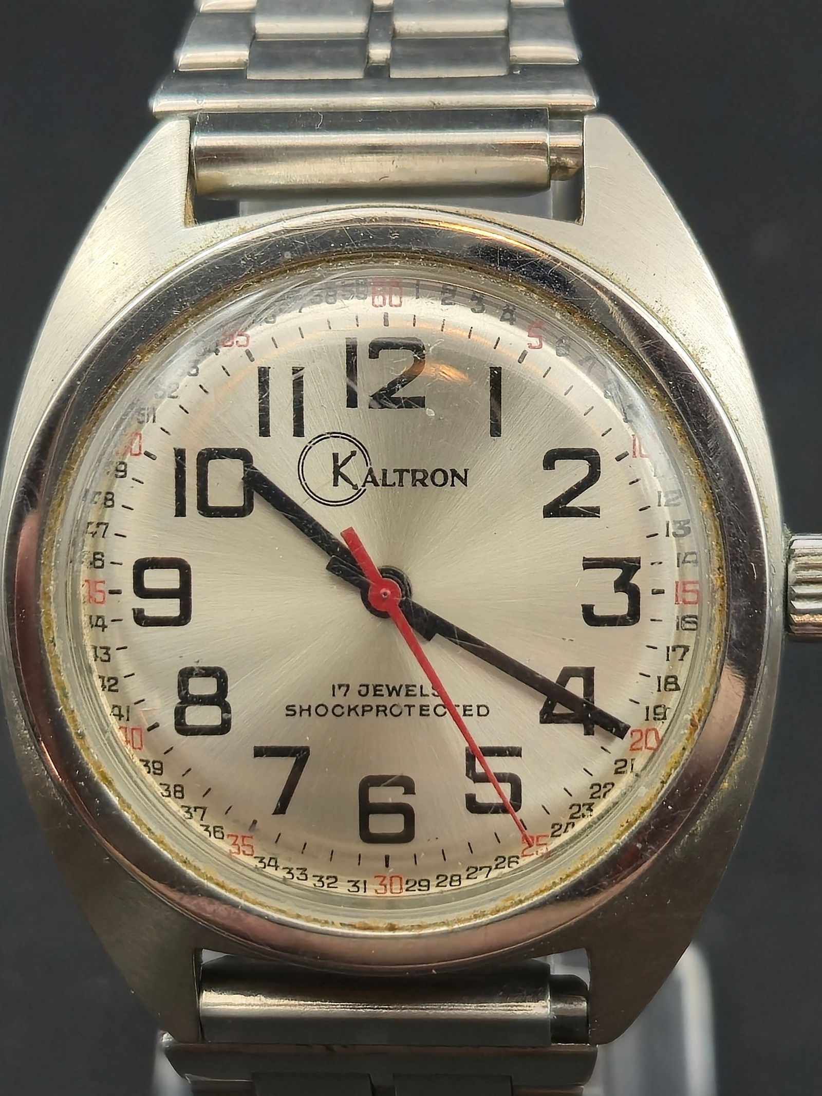 1960s Kaltron 17 Jewel Shockprotected Manual Wind 35mm Stainless Steel: Vintage Kaltron manual wind wristwatch featuring a clean silver sunburst dial with bold Arabic numerals, red sweep seconds hand, and inner 24 hour track. Marked 17 Jewels Shockprotected on the dial. S