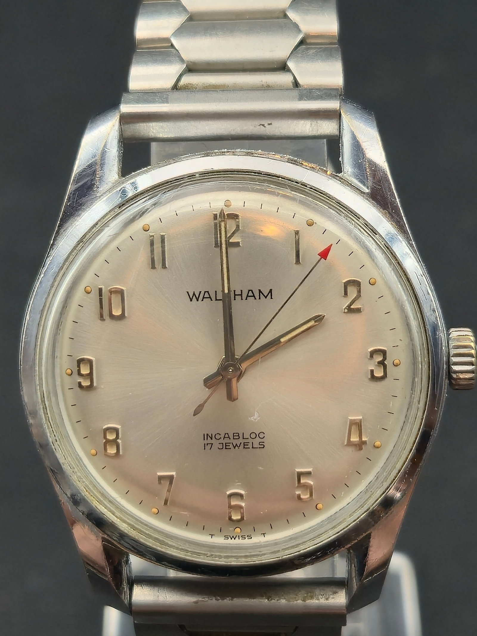 1960s Waltham Incabloc 17J Swiss Made Stainless Steel 34mm Red Arrow Seconds: Vintage Waltham Swiss-made wristwatch featuring a silver sunburst dial with applied gold Arabic numerals, Incabloc shock protection, and 17-jewel mechanical movement. Red arrow seconds hand and T Swis
