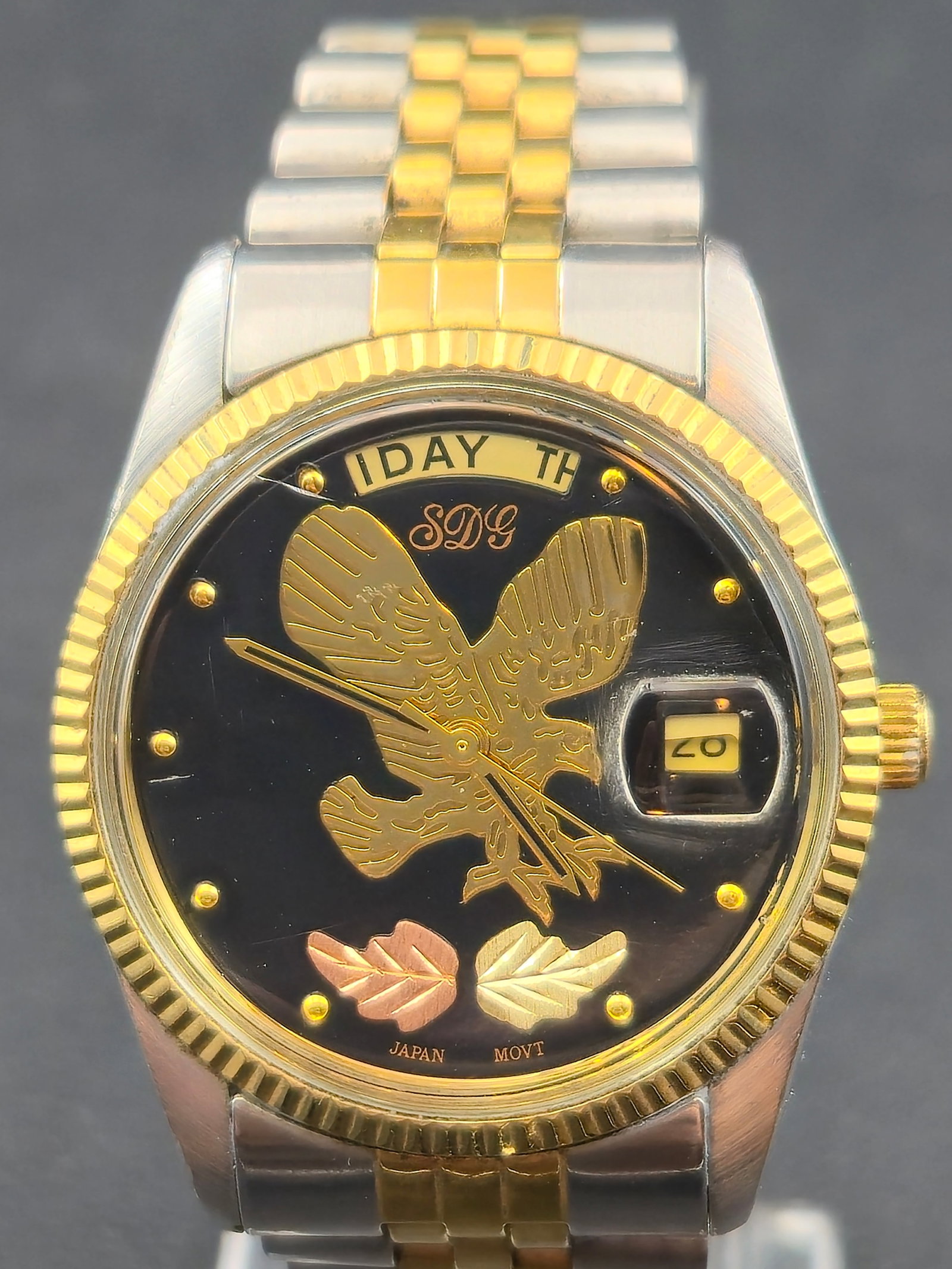 1990s SDG President Style Day Date 35mm Two Tone Steel Gold Japan Quartz Watch Running New Battery: 1990s SDG President style day date quartz wristwatch featuring a black dial with raised gold tone eagle motif, applied gold markers, day display at 12, and magnified date at 3. Dial marked SDG and Jap