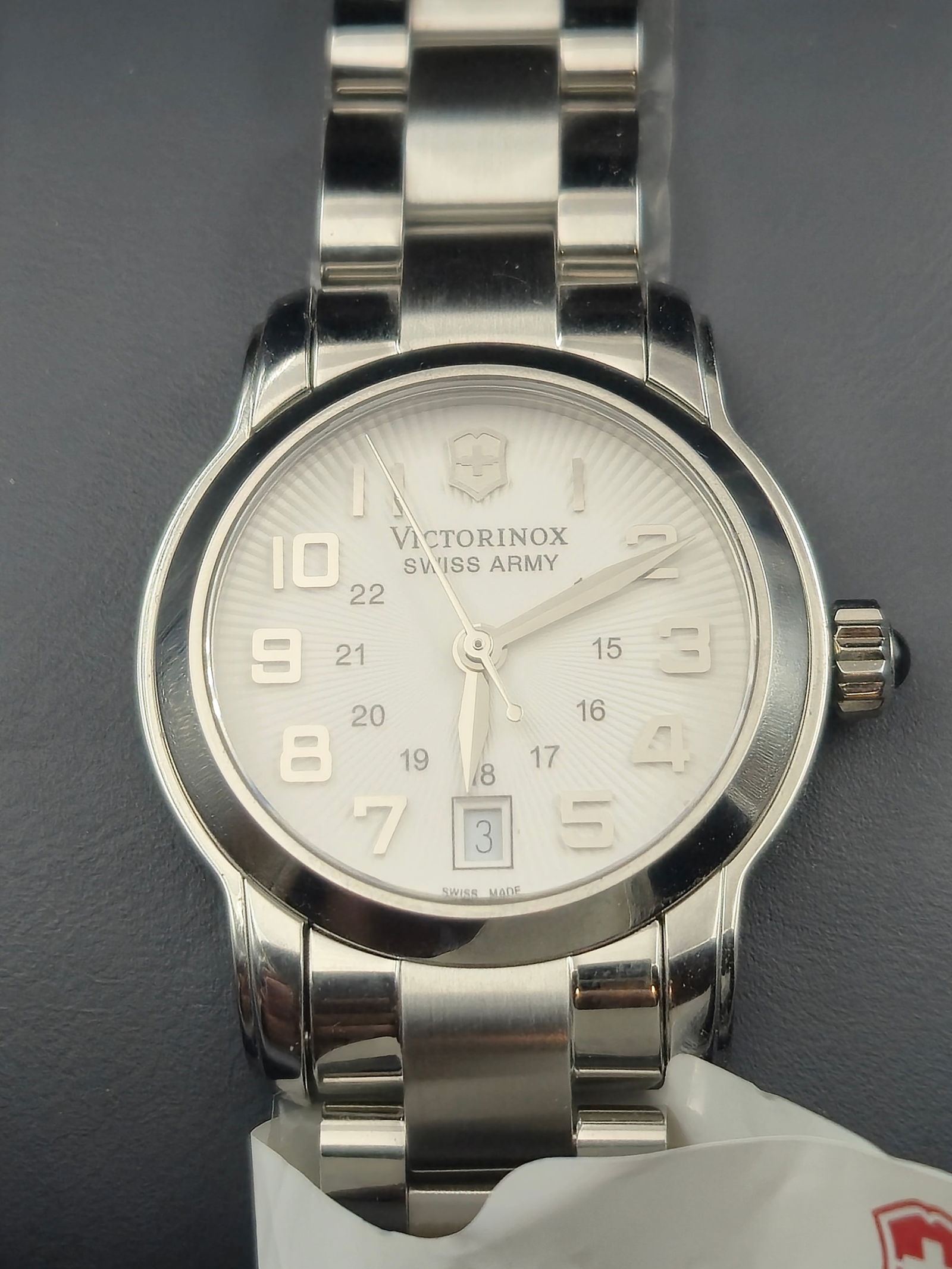 NOS Victorinox Swiss Army 241068 28mm Sapphire 100M Steel Quartz New Battery Box: New old stock Victorinox Swiss Army reference 241068 stainless steel quartz wristwatch featuring silver sunburst dial with applied Arabic numerals, inner 24-hour track, and date at 6 o’clock. Sapphi