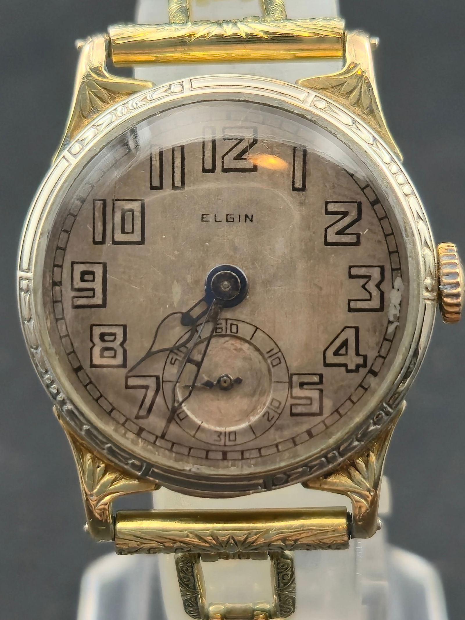 1928 Elgin Art Deco Wristwatch 27mm 14K Gold Filled Wadsworth Case Subseconds Running: Vintage Elgin wristwatch from the late 1920s Art Deco era, featuring a silver dial with bold stylized Arabic numerals and a subseconds register at the 6 o’clock position. The watch has ornate engrav