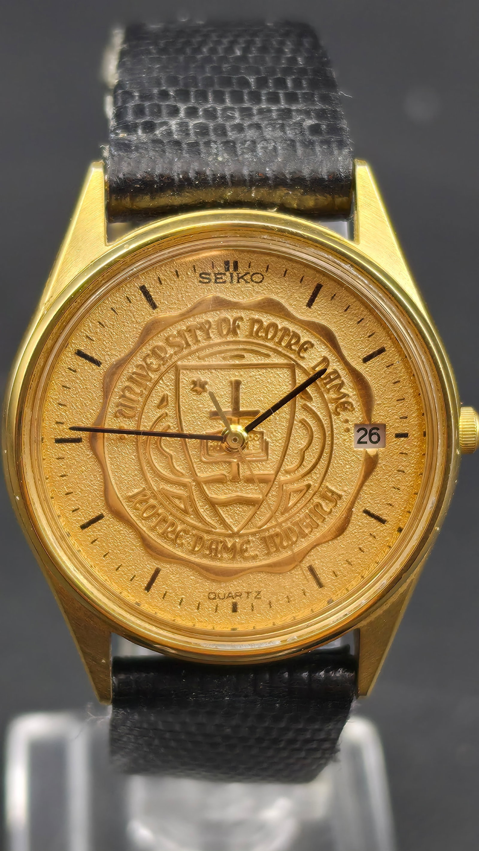1988 Seiko Quartz 5Y22-7009 34mm Gold Tone Notre Dame Seal Dial Watch New Battery: Seiko quartz wristwatch featuring a rare embossed Notre Dame themed seal dial with gold tone case. Dial signed Seiko with “University of Notre Dame” crest design and date window at 3. Caseback