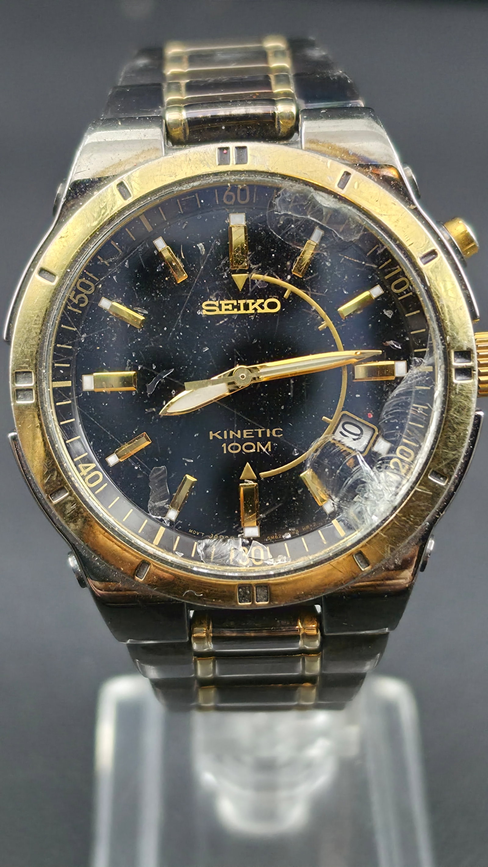 Seiko Kinetic 100M Two Tone 39mm Black Dial Date Watch Runs Original Bracelet: Seiko Kinetic wristwatch featuring a black dial with gold-tone markers, date display at 3 o’clock, and 100M water resistance. Two-tone stainless steel case and bracelet with gold accents. Measures a
