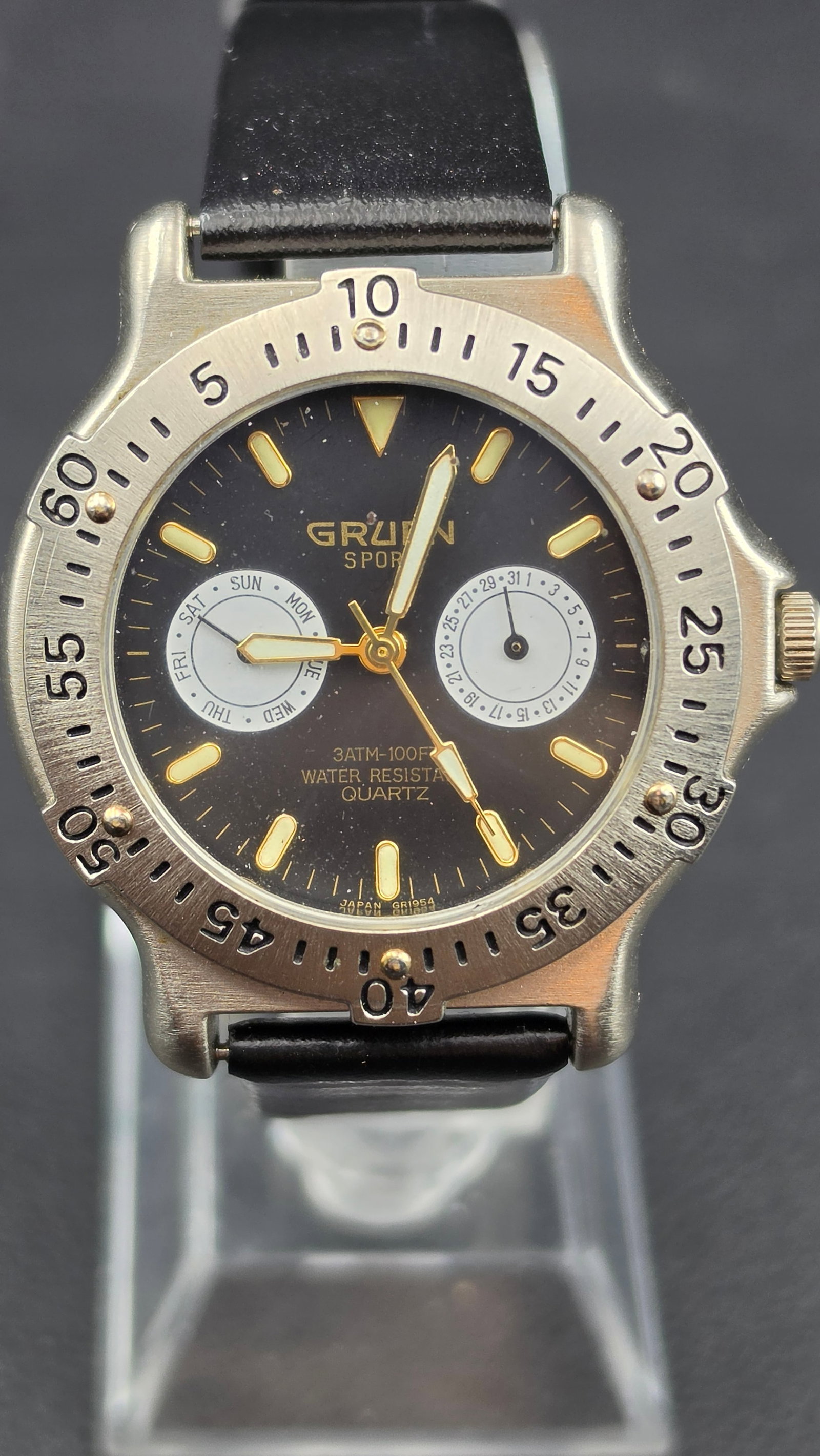 Gruen Sport Diver Style Day Date Quartz Watch 38mm 293-VX36 Black Dial Running: Gruen Sport quartz wristwatch featuring a diver-style rotating bezel and dual subdial layout for day and date display. Black dial with luminous markers and gold-tone hands, housed in a stainless steel